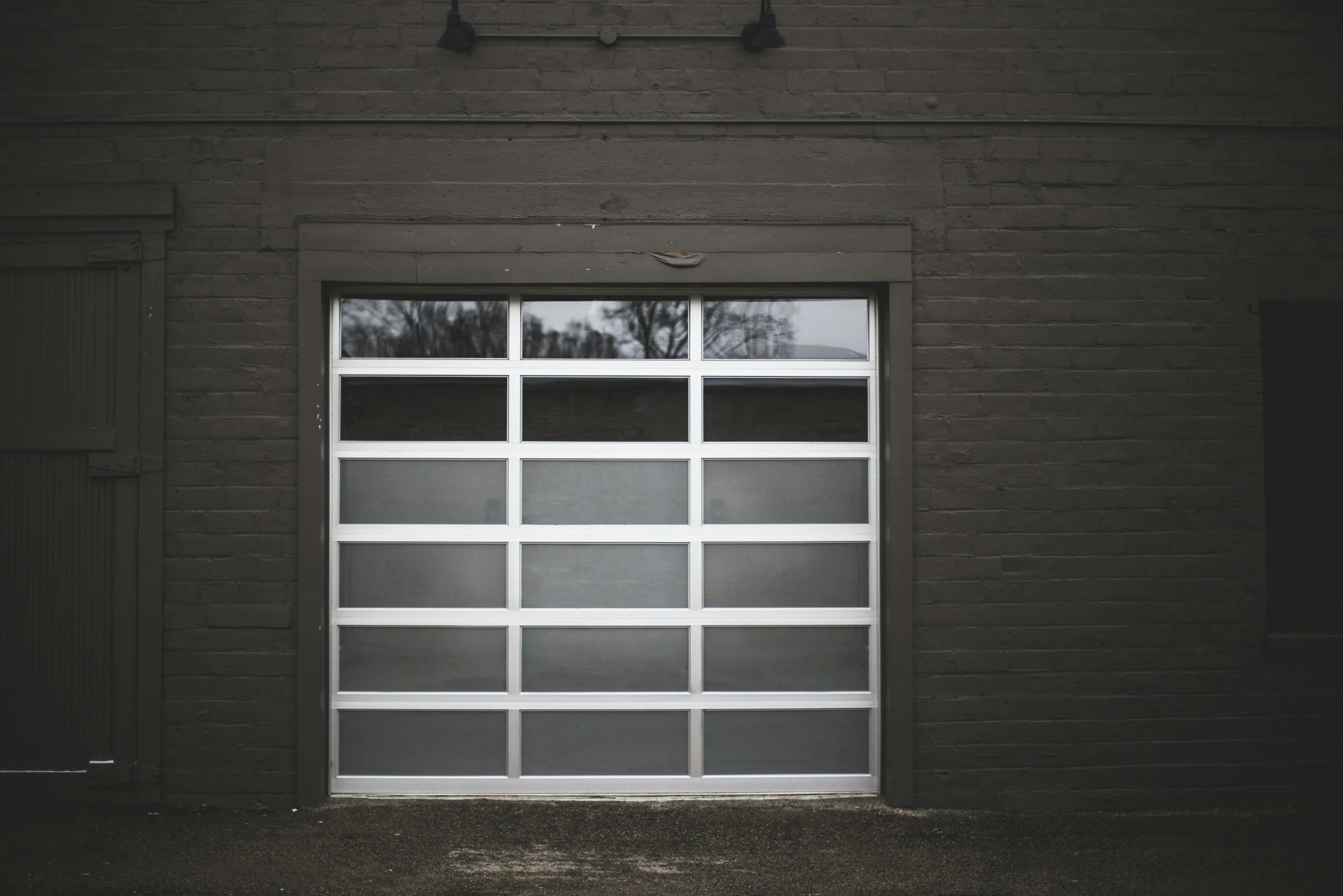 Gray metal garage door with glass panels on a dark brick wall exterior.