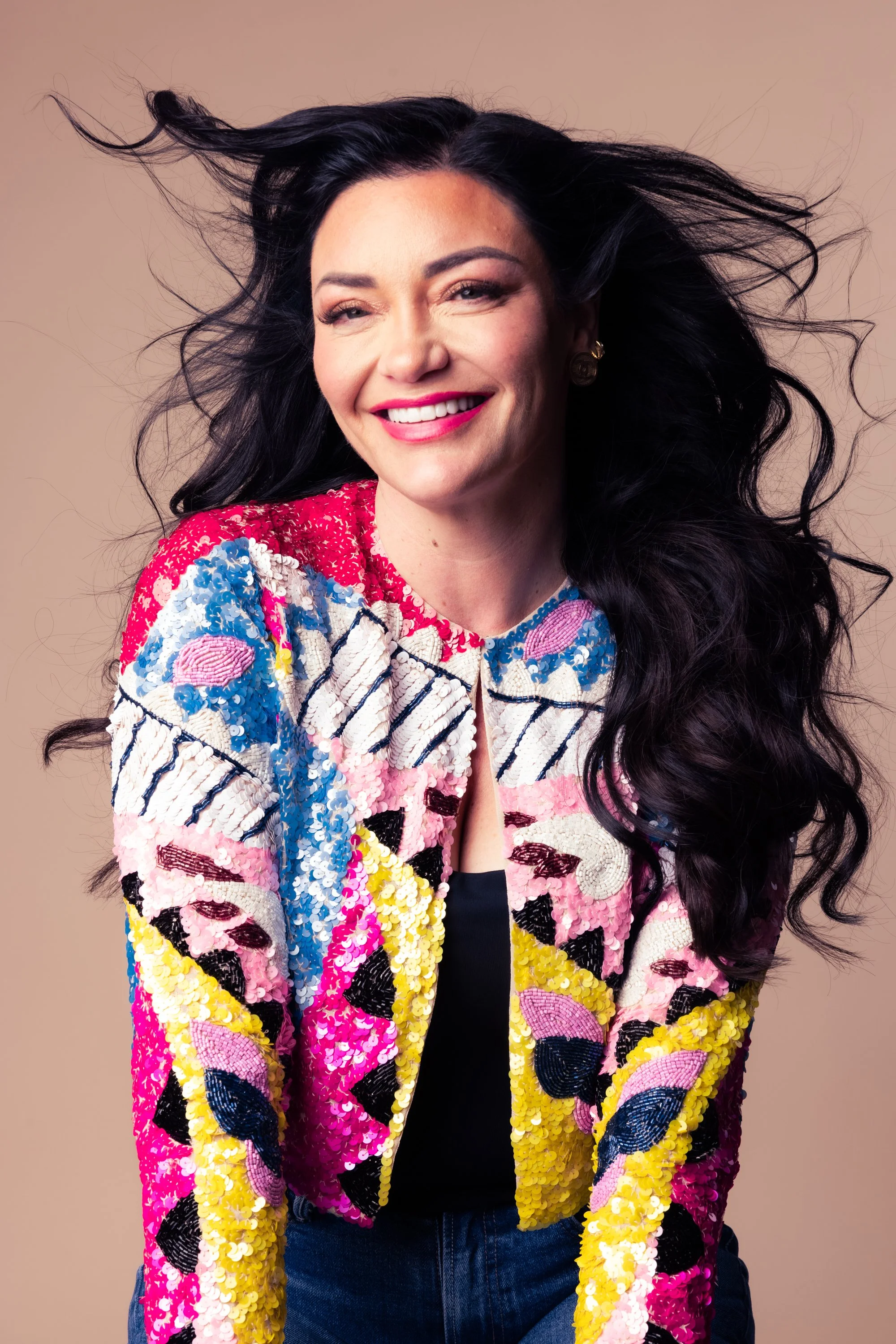 Smiling woman with long black hair wearing a colorful sequined jacket.
