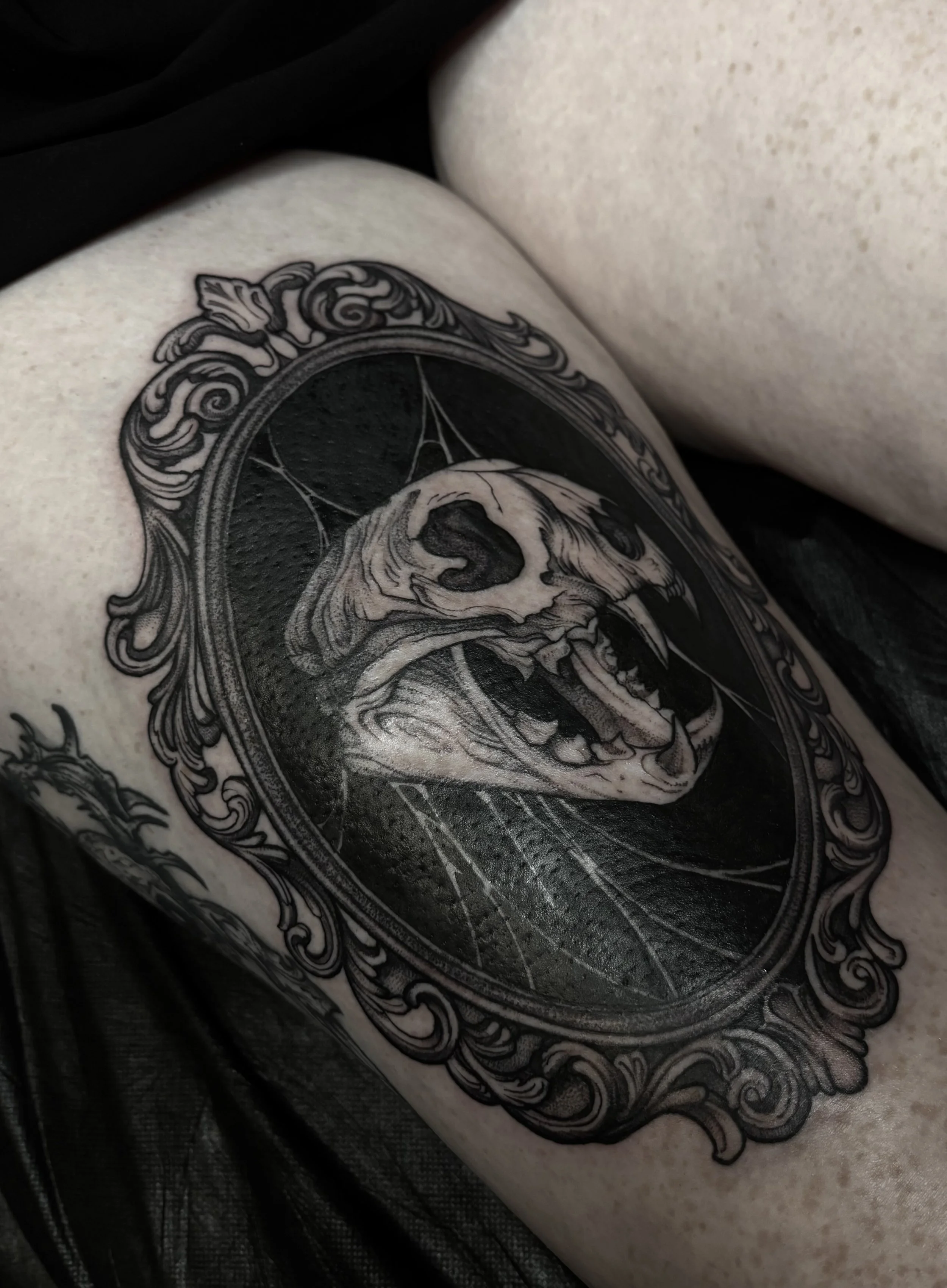 A black and white tattoo of a bear skull surrounded by ornate decorative elements on a person's upper arm.