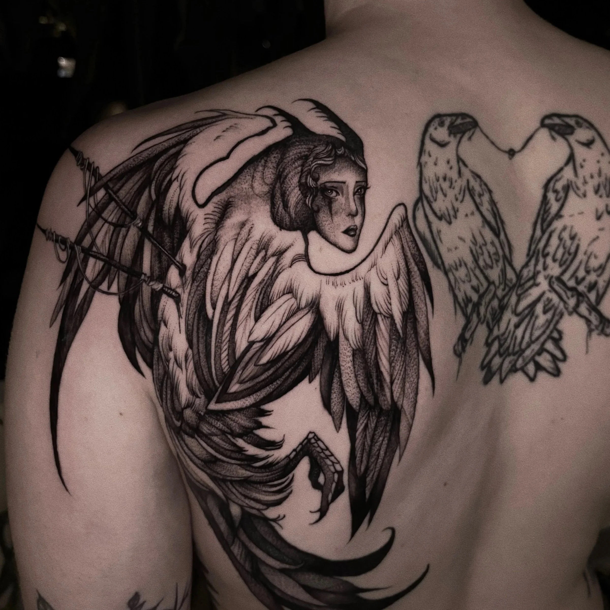 Black line art tattoo of a woman with long hair and angel wings on a person's upper arm.