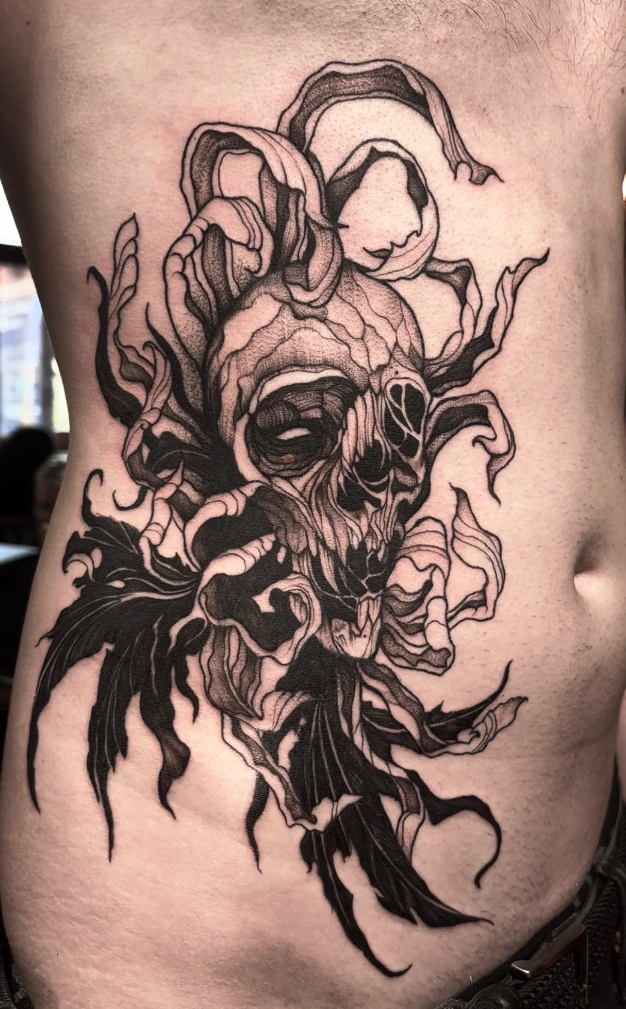 A black and gray tattoo of a stylized roaring lion's face with intricate line work and shading on a person's side torso.