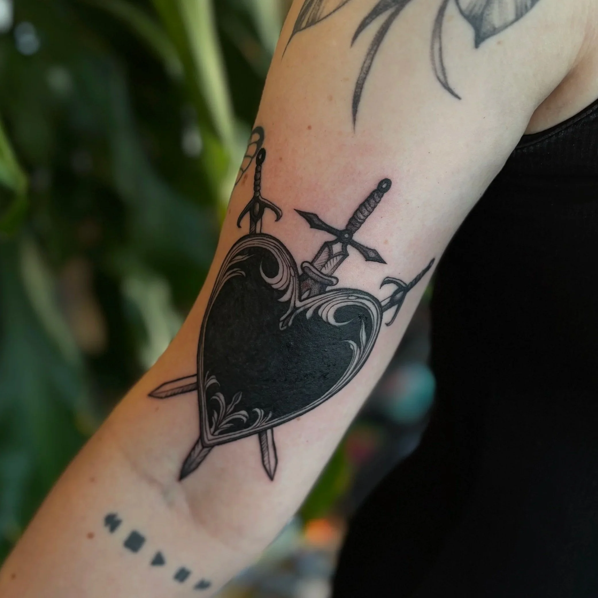 Close-up of a tattoo on a person's arm featuring an anchor and a nautical theme, with some green leaves in the background.