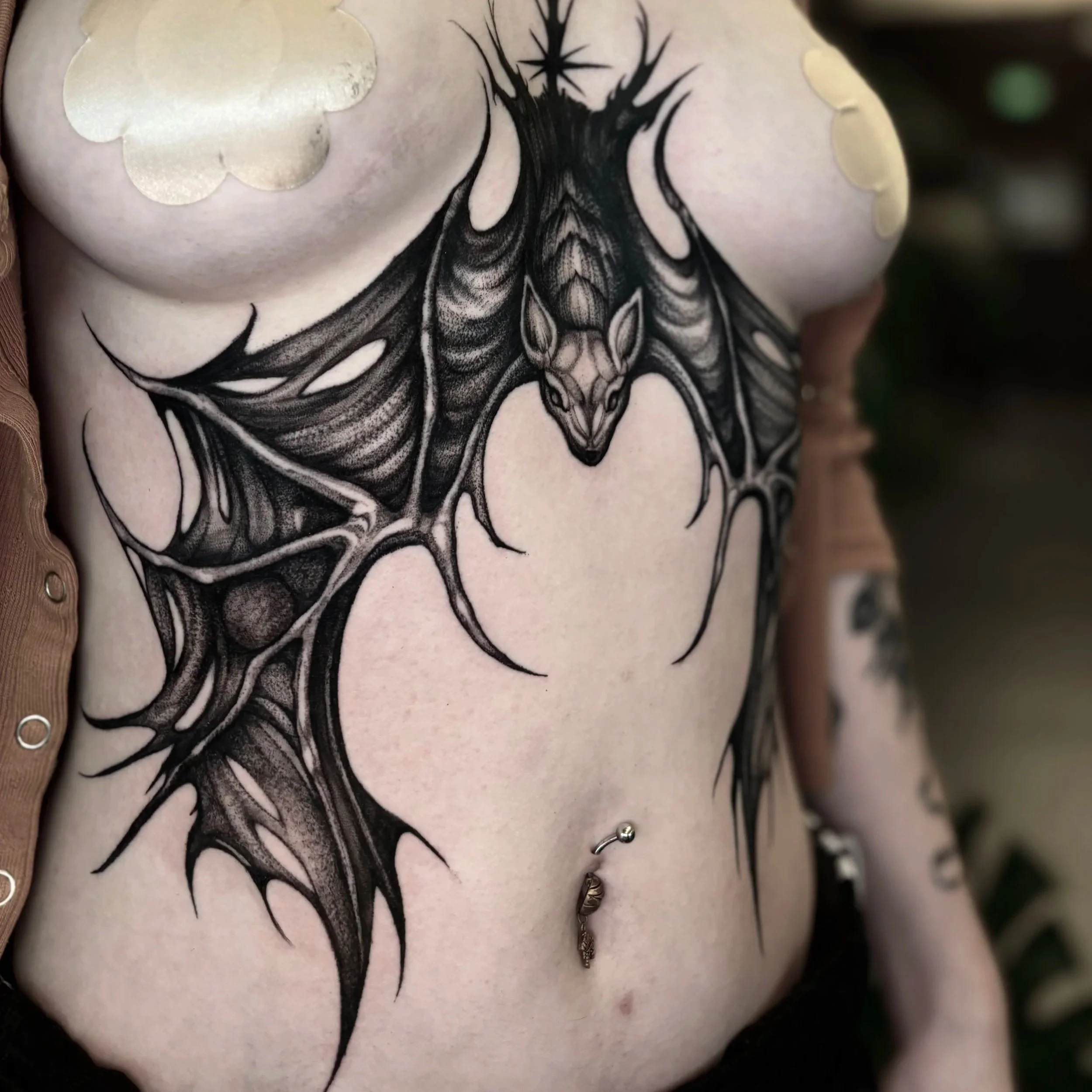 Black ink tattoo of a spider with multiple legs and a detailed body, located on a person's chest, with some skin visible around it.