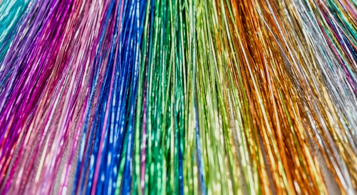 Close-up of metallic colorful fairy tinsel hair strands arranged side by side in rainbow order.