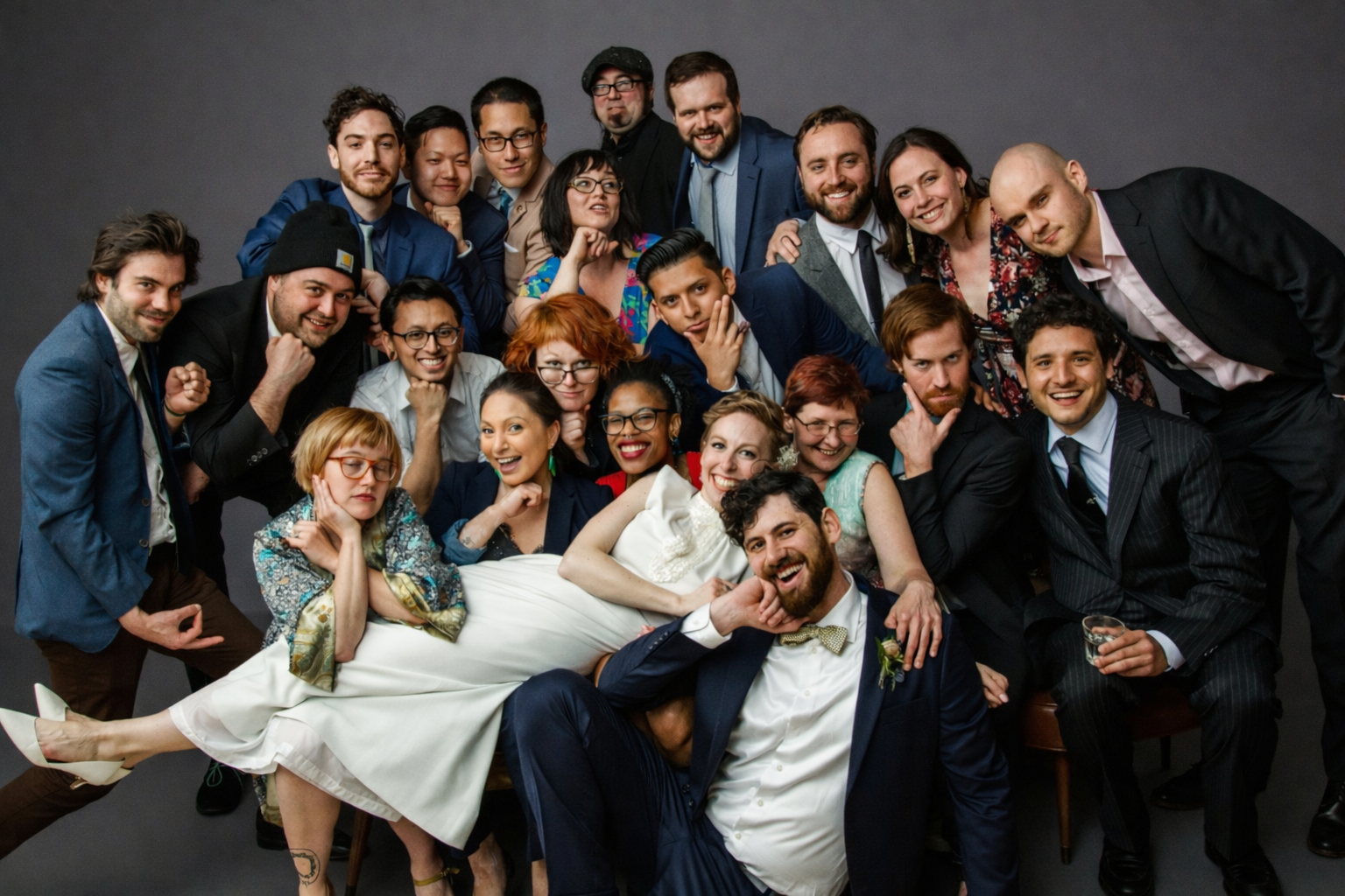 Team posing for a photo, with one person lying across others in front, all smiling against a dark background.