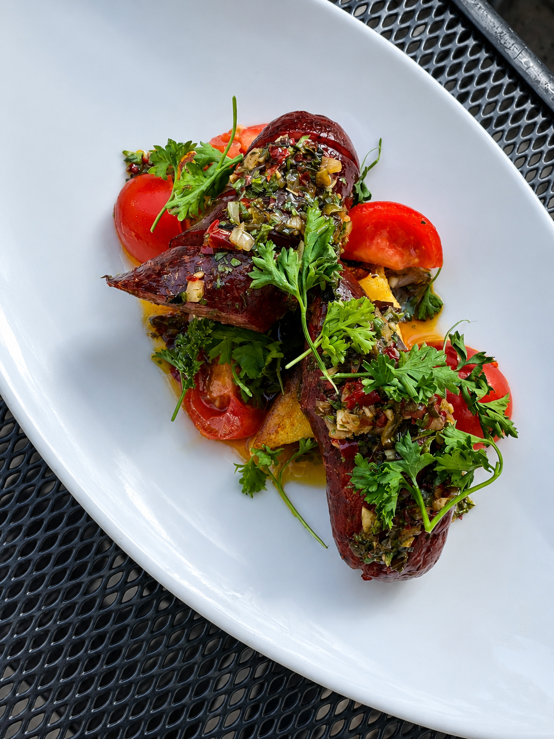 A plate of stuffed peppers topped with chopped herbs and fresh parsley, garnished with cherry tomatoes and greens.