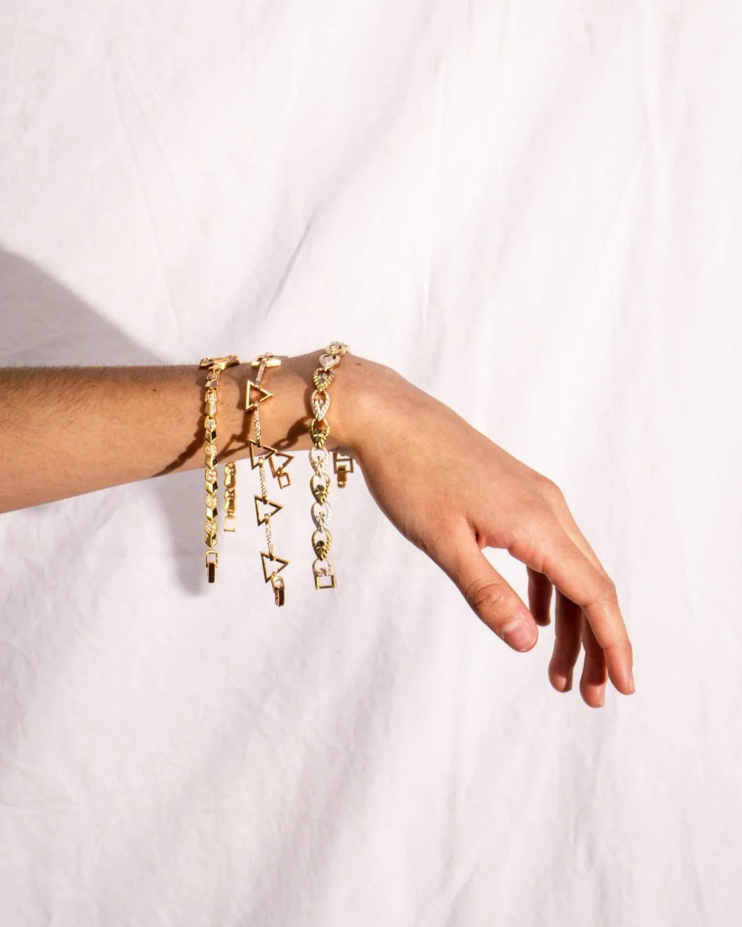 A person's left arm extended to the right, wearing four gold bracelets with geometric designs against a plain white background.