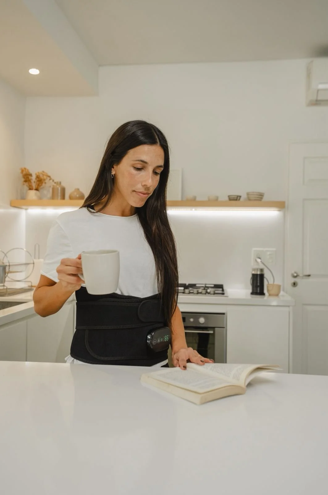 Mujer en la cocina con su Heat, sosteniendo una taza y leyendo un libro.