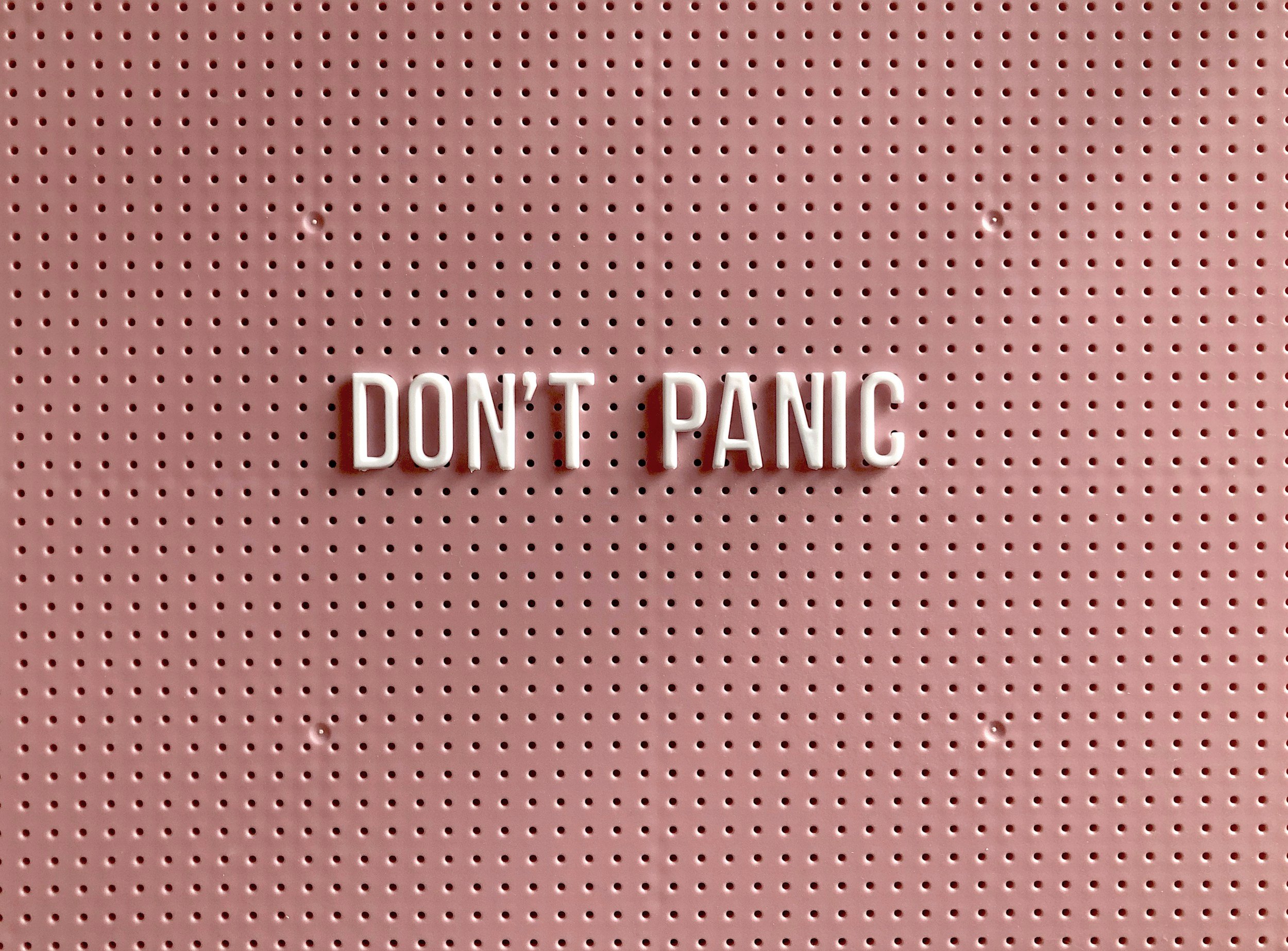 Don't Panic is written on a pink pegboard. Anxiety and perfectionism often create panic responses.