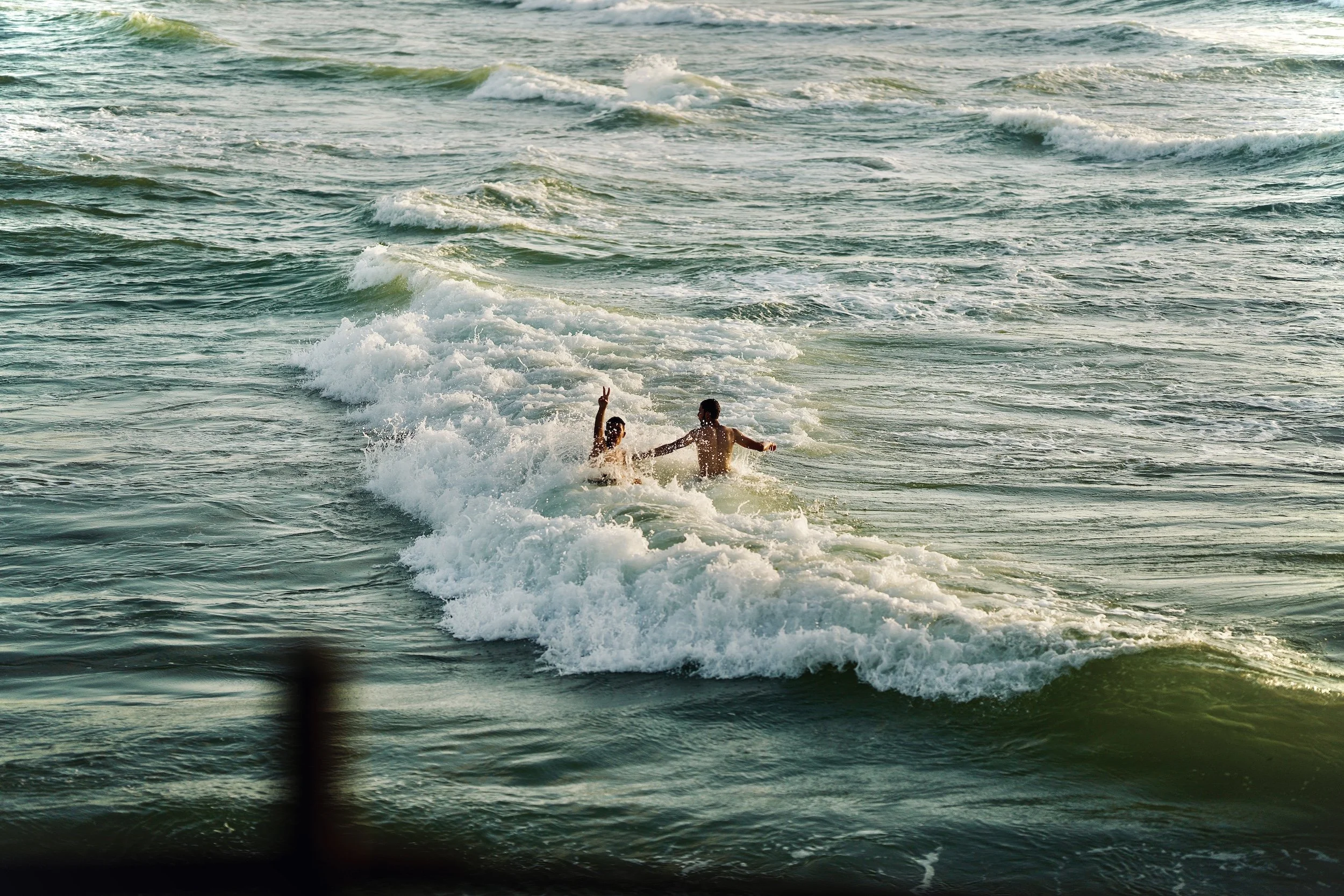 Two Palestinian men swimming and playing in the ocean waves near the shore.