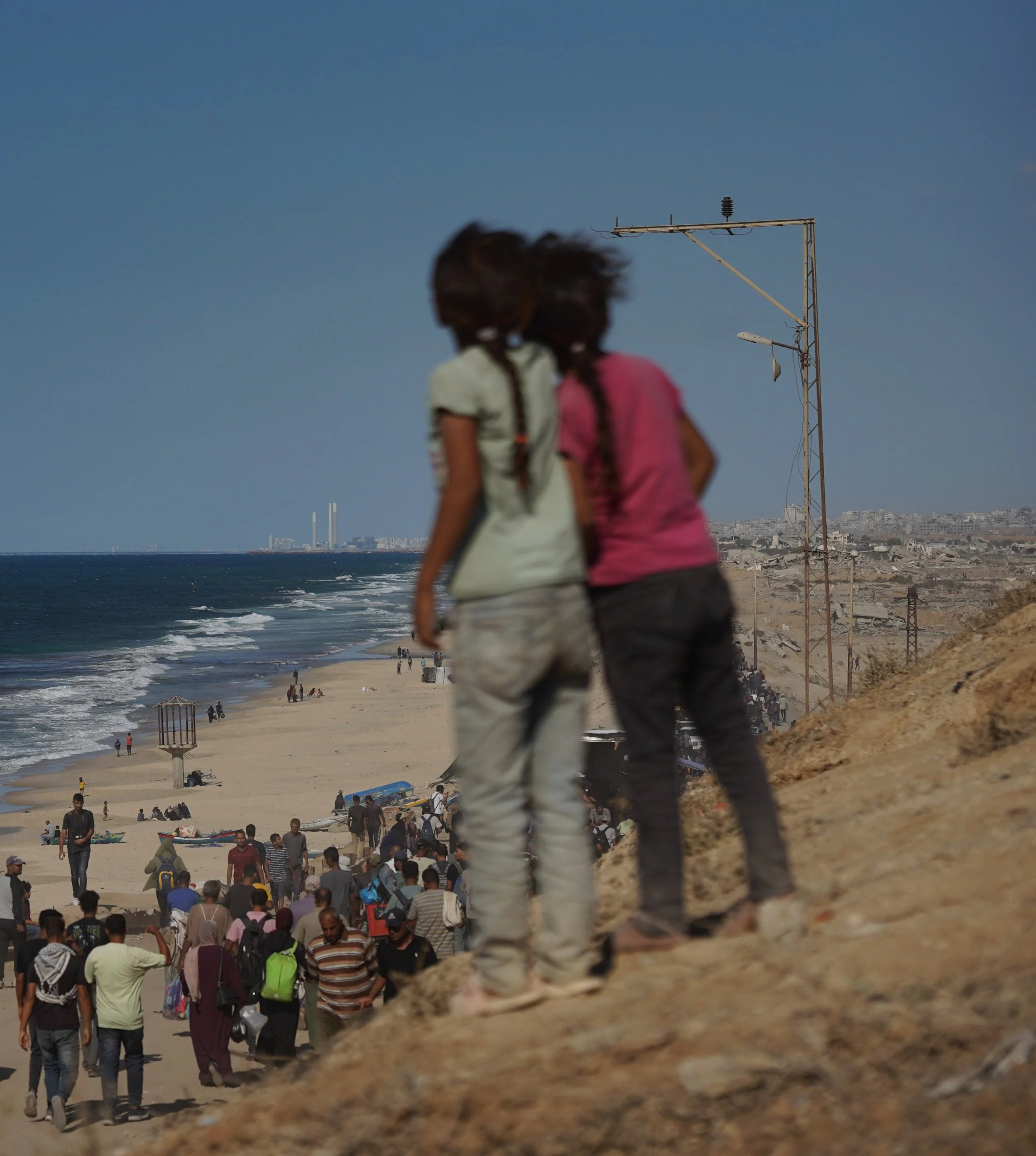 Two young Palestinian girls observe a crowd of Palestinians walking north along the Gaza coast.