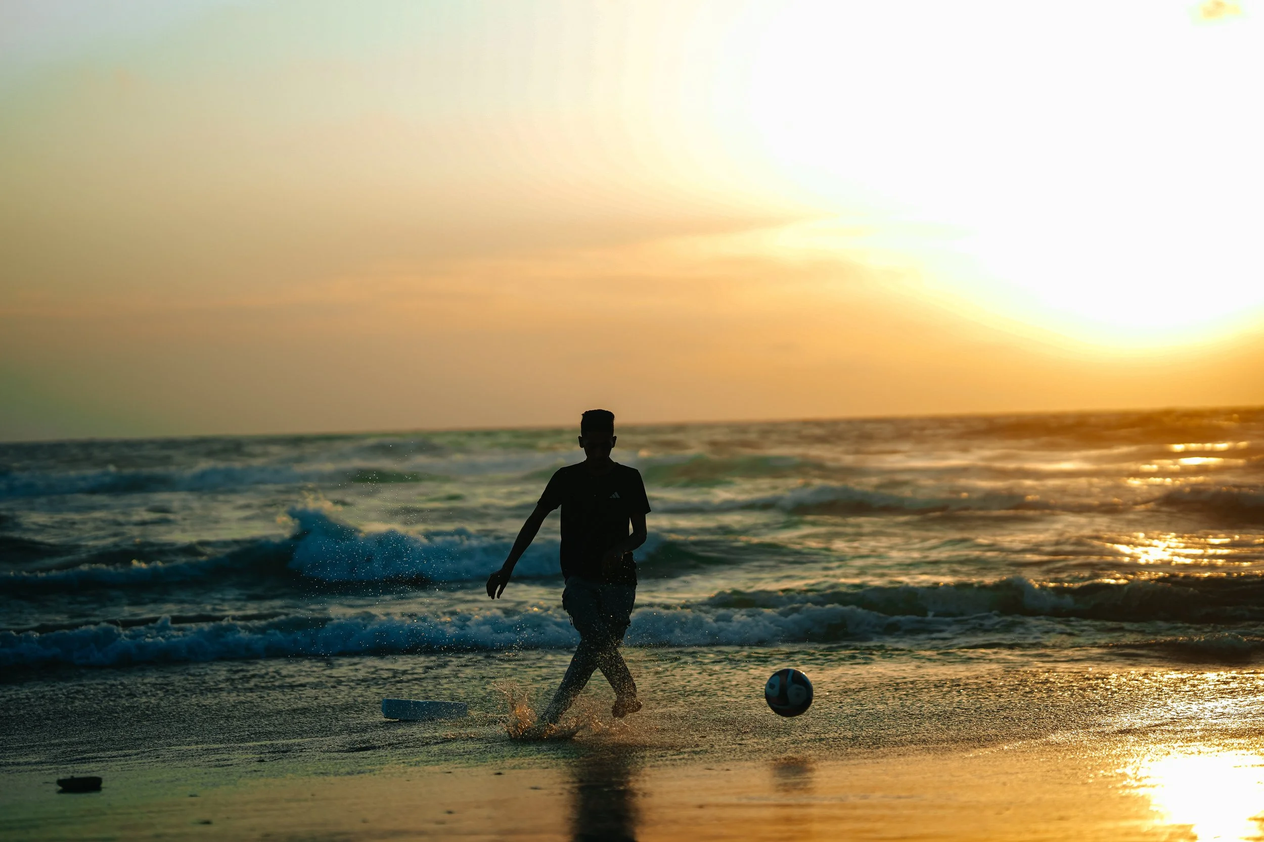 A young boy playing soccer on the beach in Gaza at sunset.