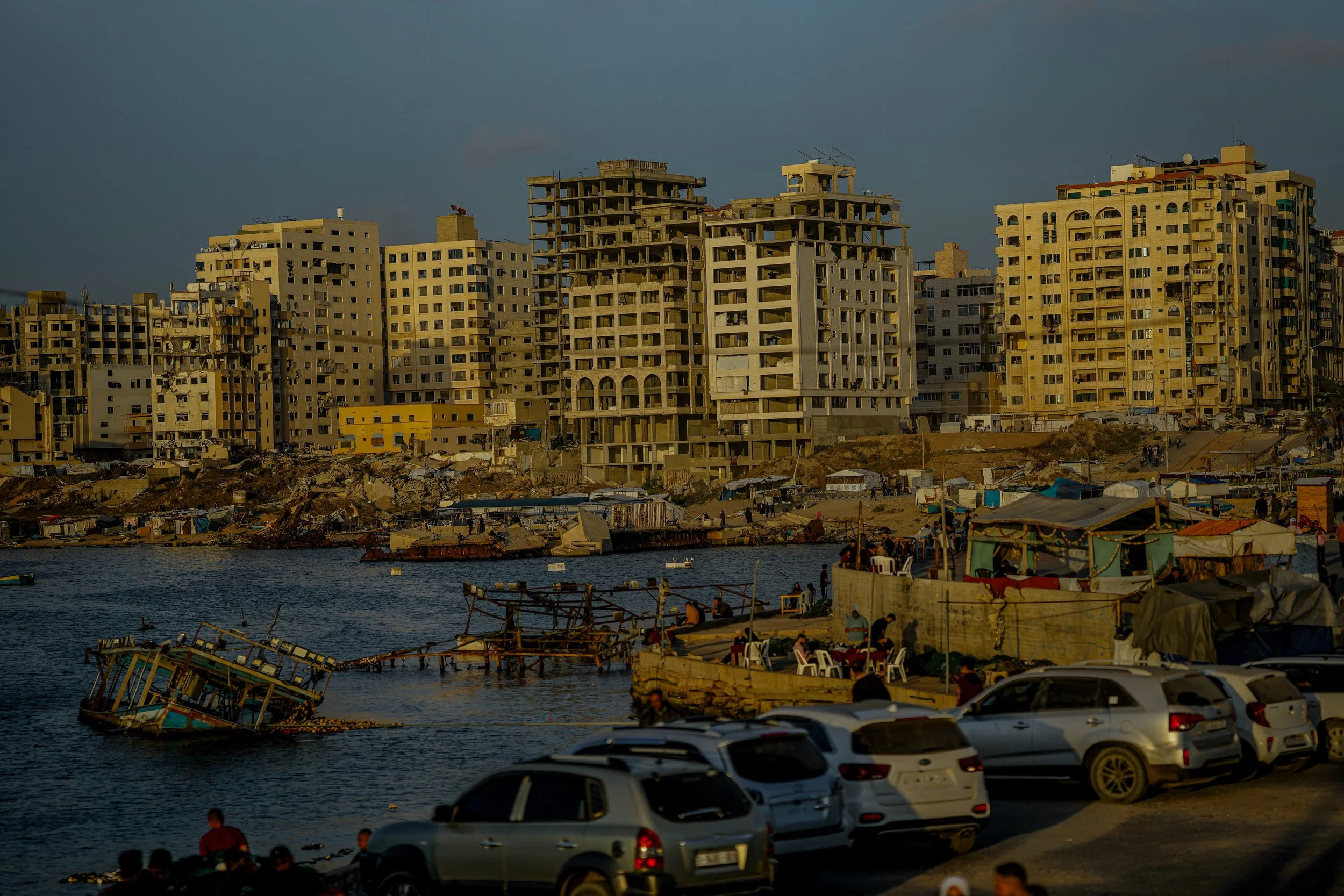 Cityscape of Gaza with high-rise buildings under a cloudy sky, and a view of the port.
