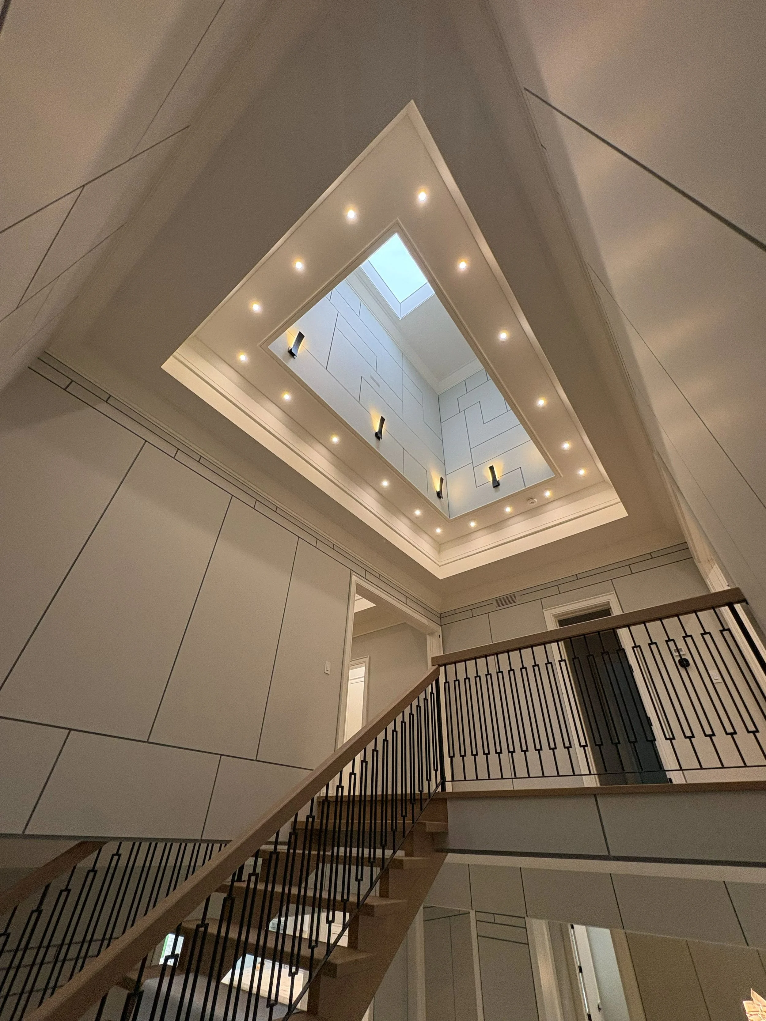 Interior view of a multilevel staircase with a railing, leading to an upper floor with white walls, a skylight, and ceiling lights.
