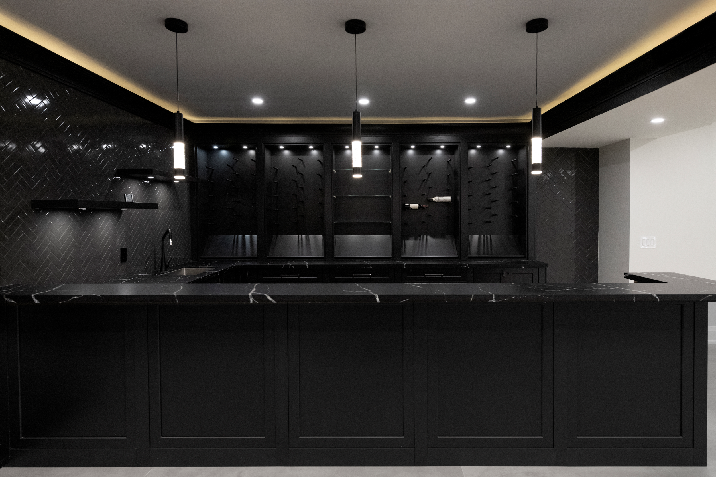 Modern black kitchen with black marble countertop, black textured wall tiles, and black cabinetry, illuminated by hanging pendant lights and recessed ceiling lights.