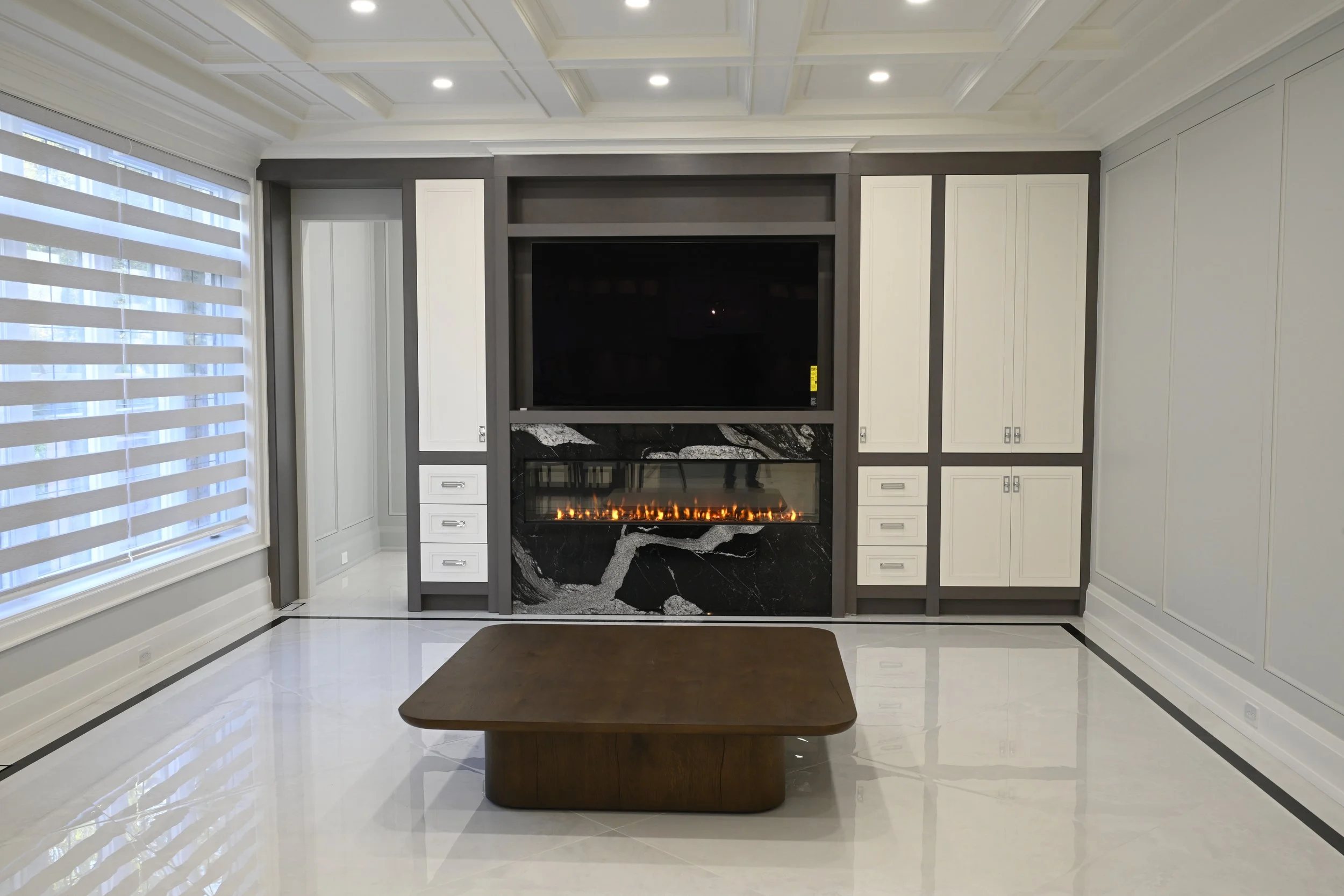 Modern living room with built-in fireplace, black marble surround, and TV above. White cabinetry and large window with striped curtains.