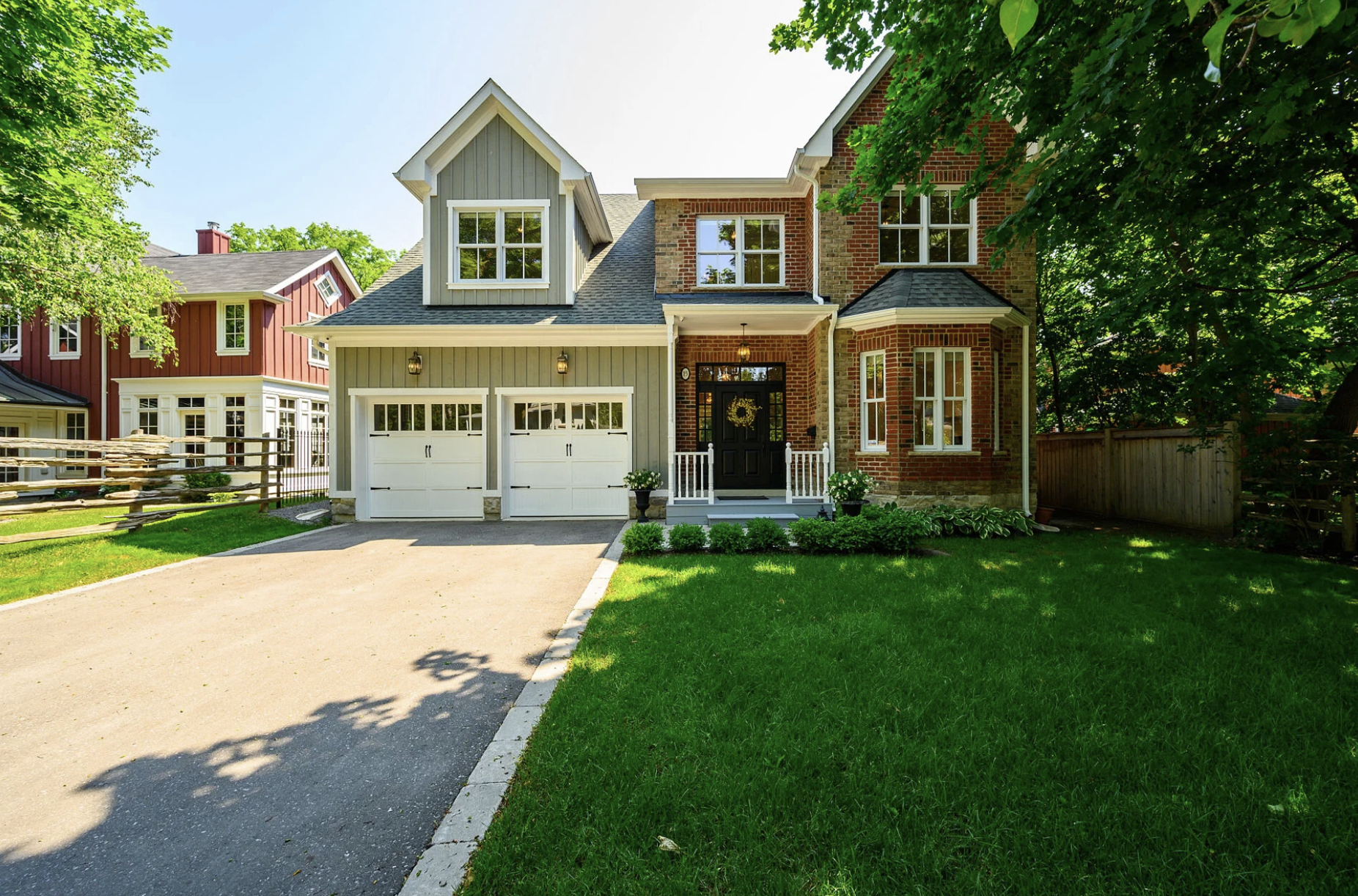 Front view of a two-story house with a mix of brick and gray siding, white trim, a double garage, and a garden with green grass and trees.