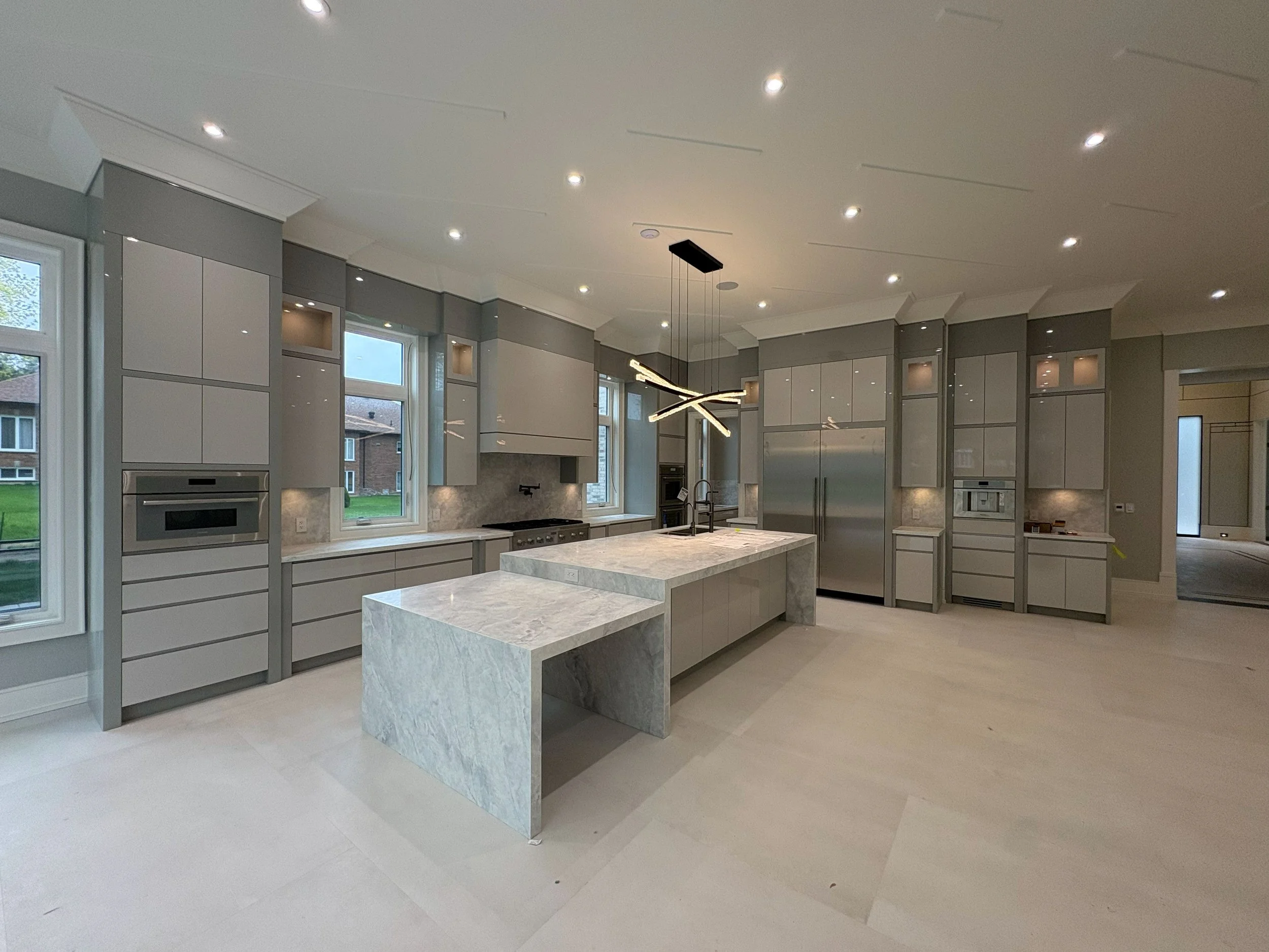Modern kitchen with white cabinets, marble island, and large windows.