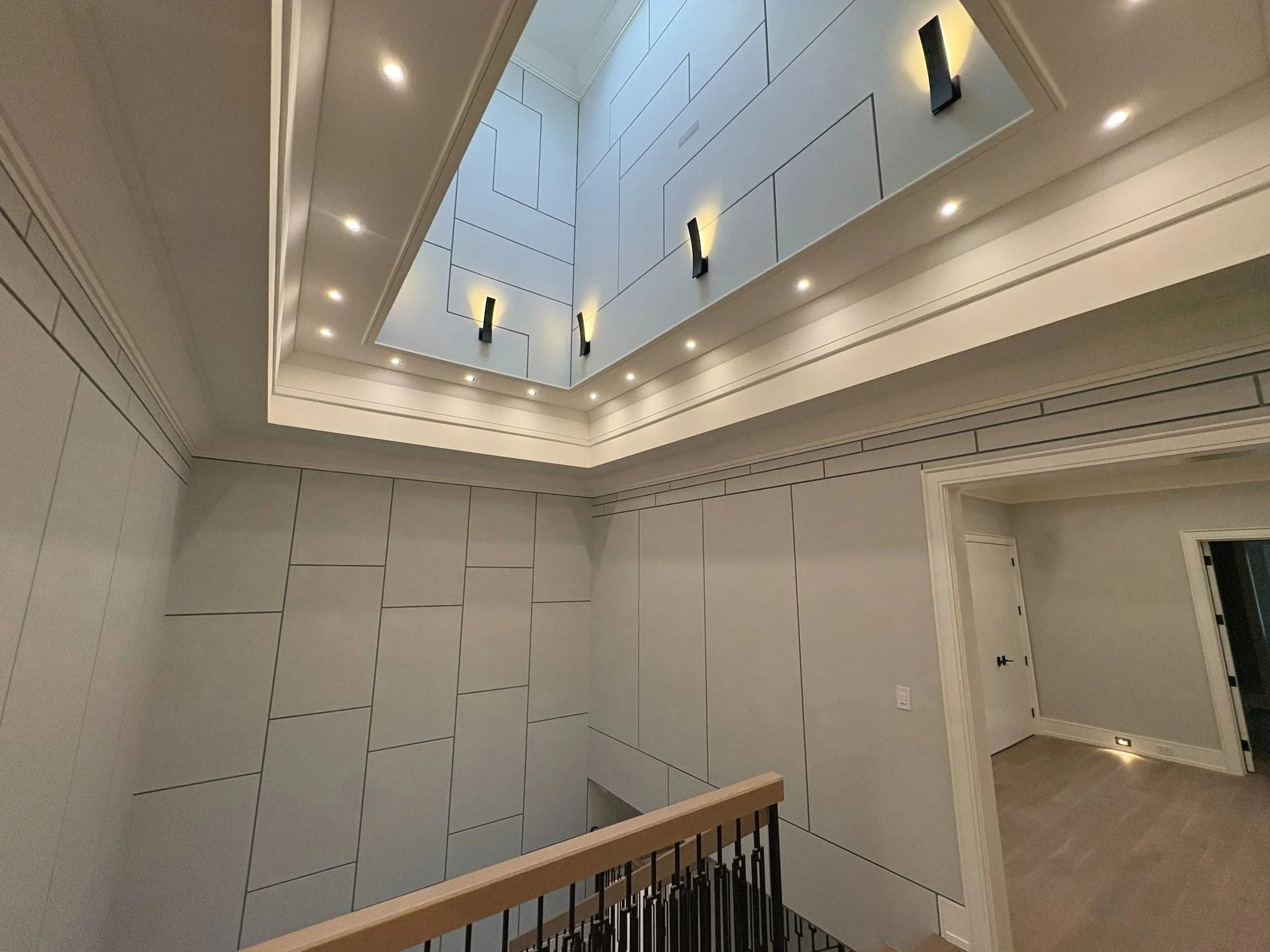 Interior view of a ceiling with recessed lighting, decorative wall paneling, and modern wall sconces illuminating the space.