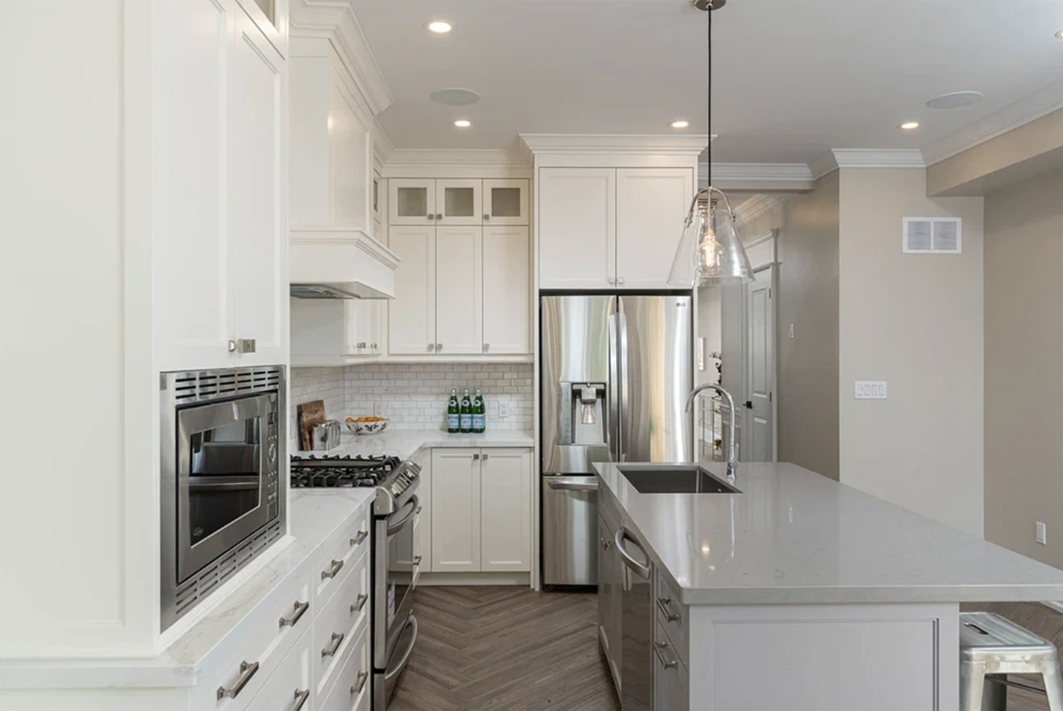 Modern kitchen with white cabinets, stainless steel appliances, island with a sink, pendant light, and light hardwood flooring.