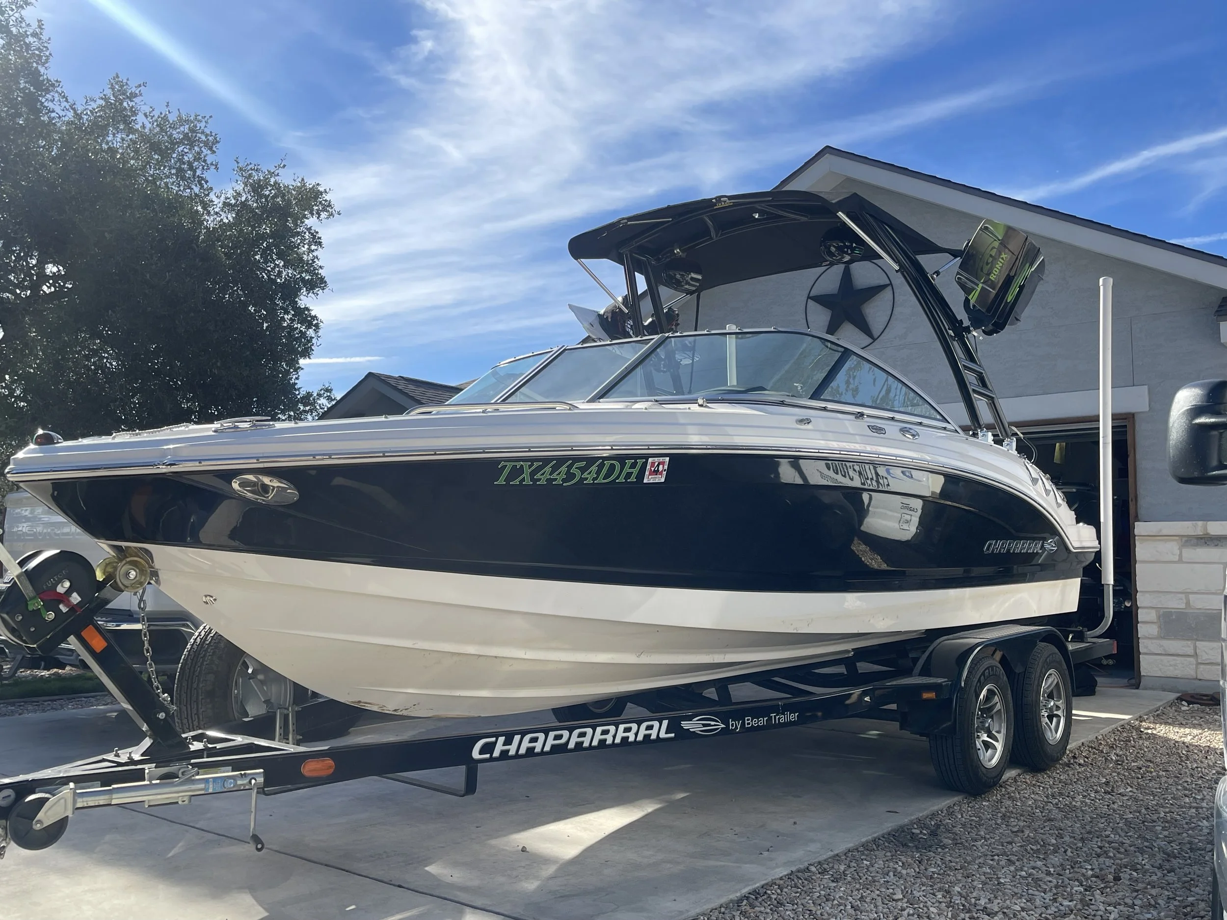 A black and white speedboat on a trailer outside a house with a driveway and a clear sky.