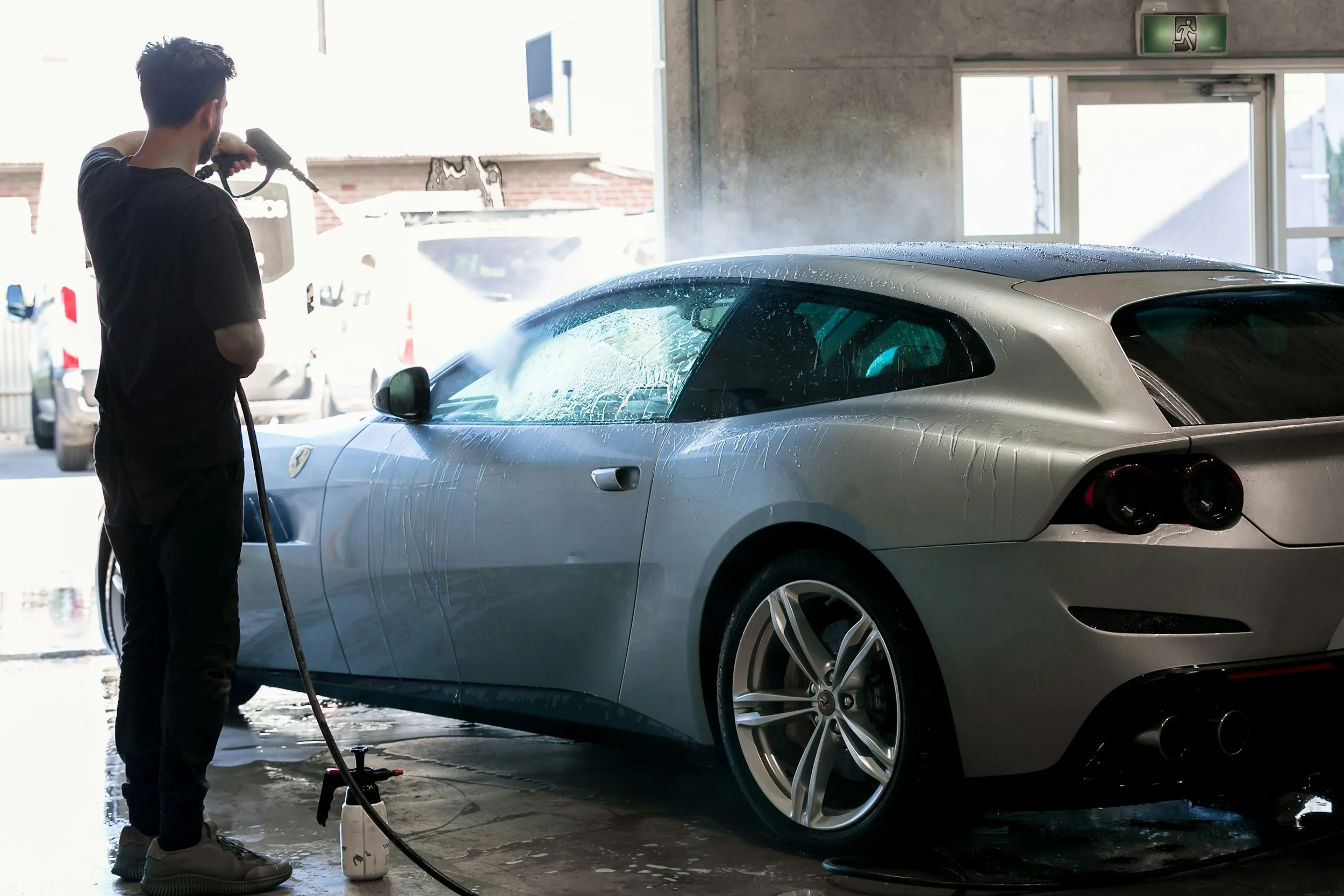 A man washing a silver sports car inside a garage.