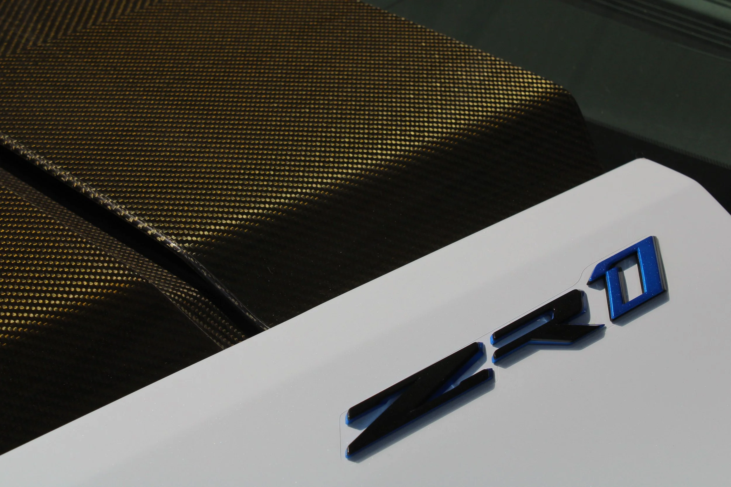 Close-up of a car's rear with a metallic carbon fiber spoiler and the letters "Z O" in black and blue on the white body.