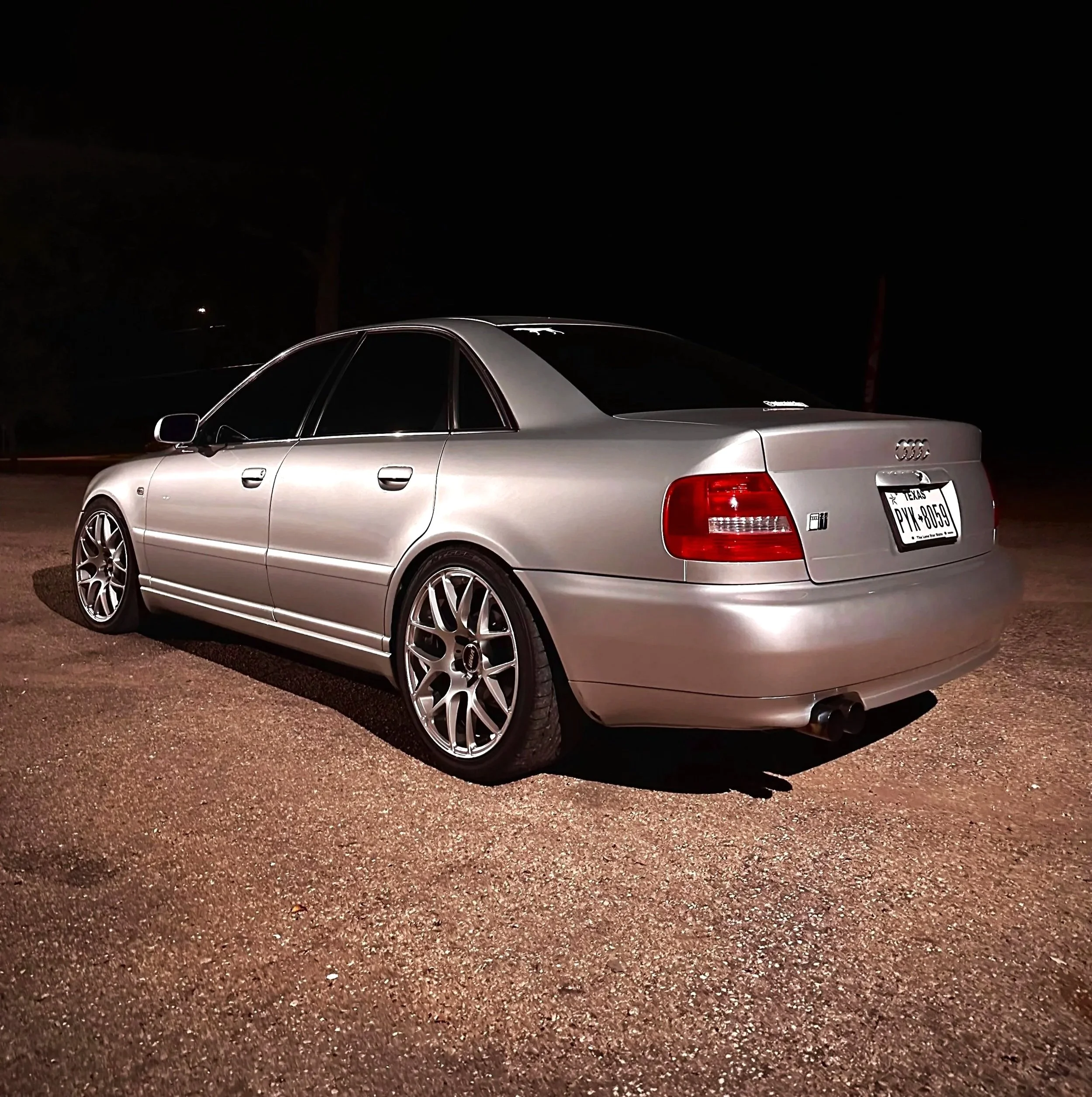 Silver Audi sedan parked on a gravel surface at night, with dark background and no visible other objects.