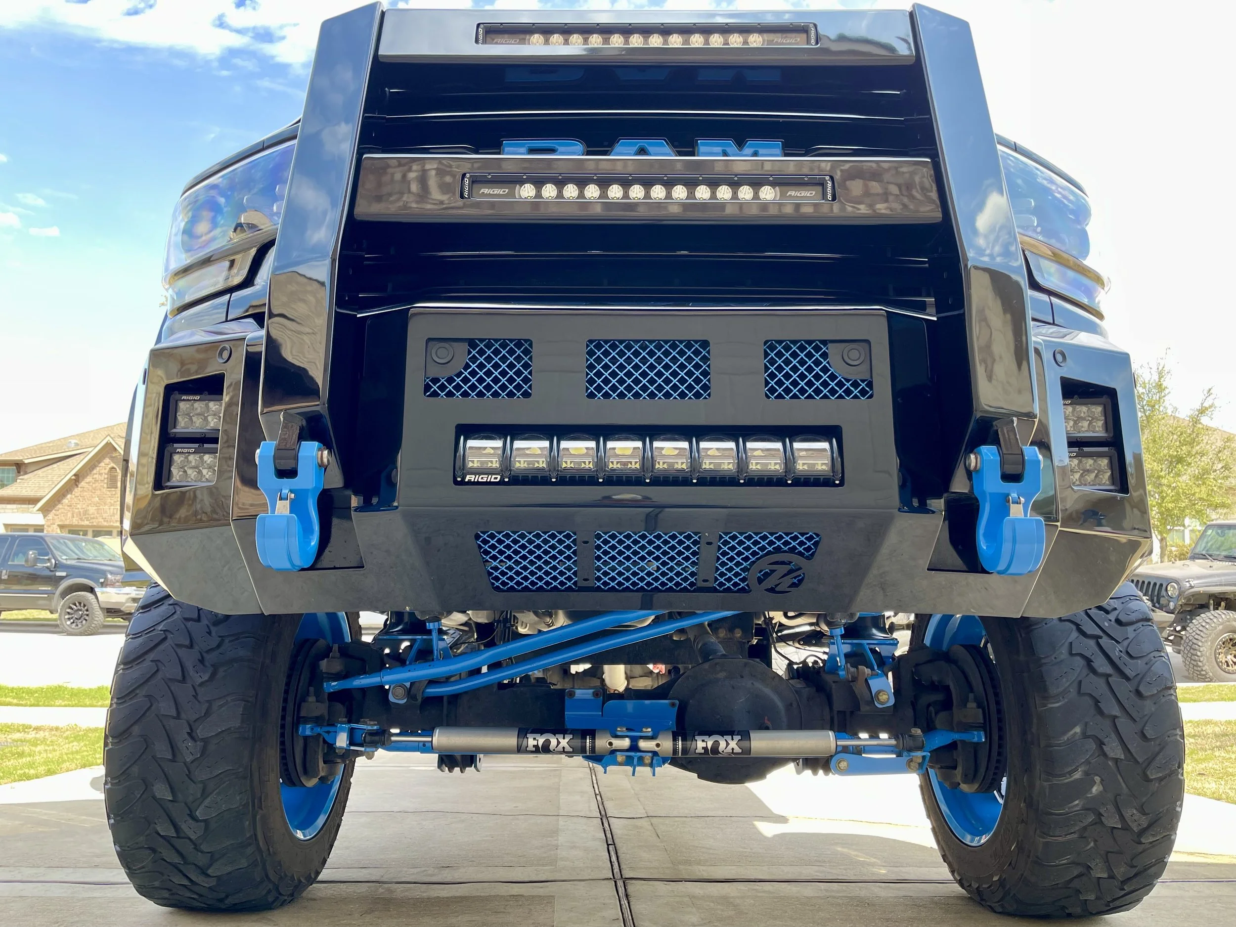 Front view of a modified black RAM truck with lifted suspension, large tires, blue accents, and auxiliary lights.