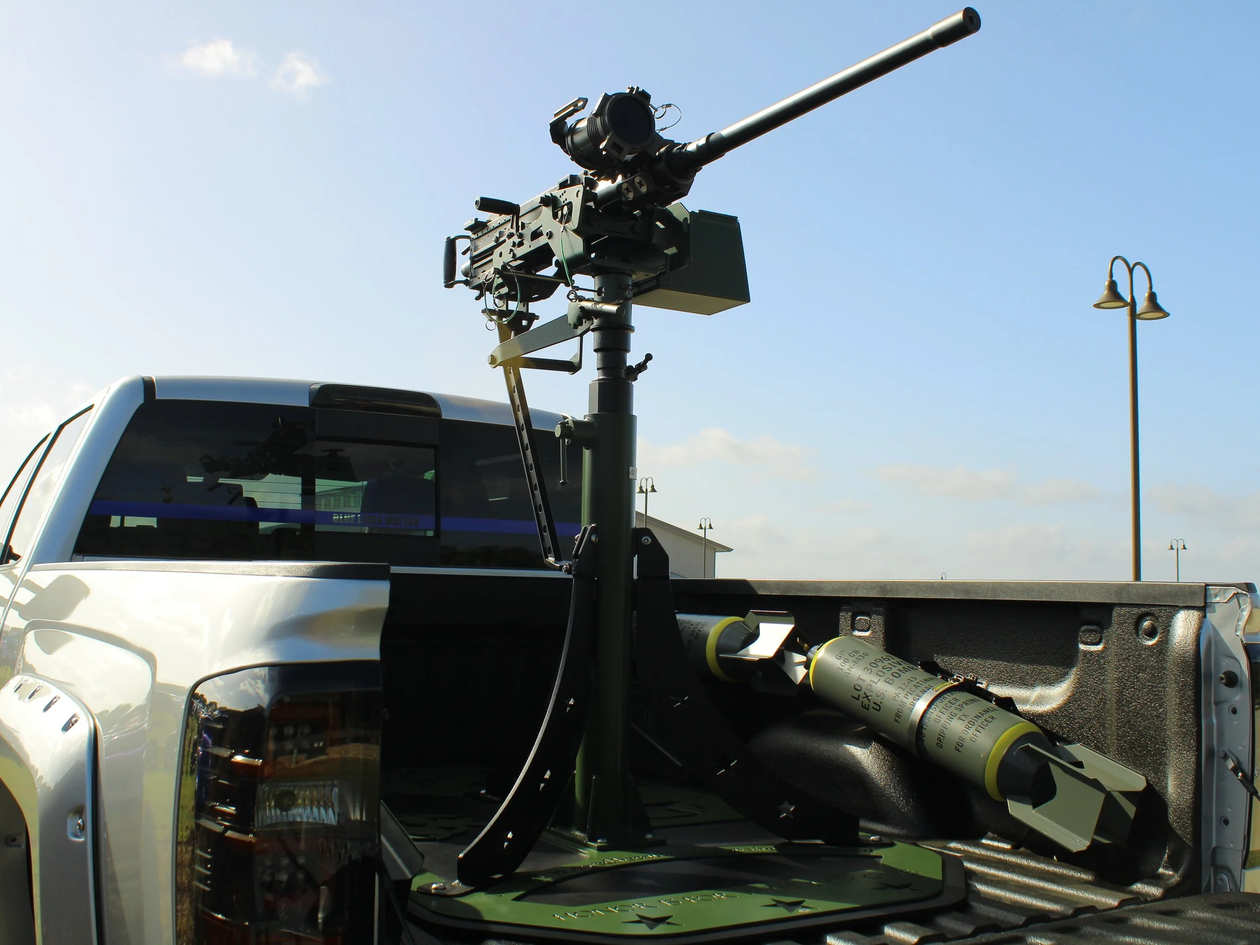 Militarized drone mounted on a truck bed, with a long barrel-like instrument and a cylindrical device, against a background of a clear sky and streetlamps.