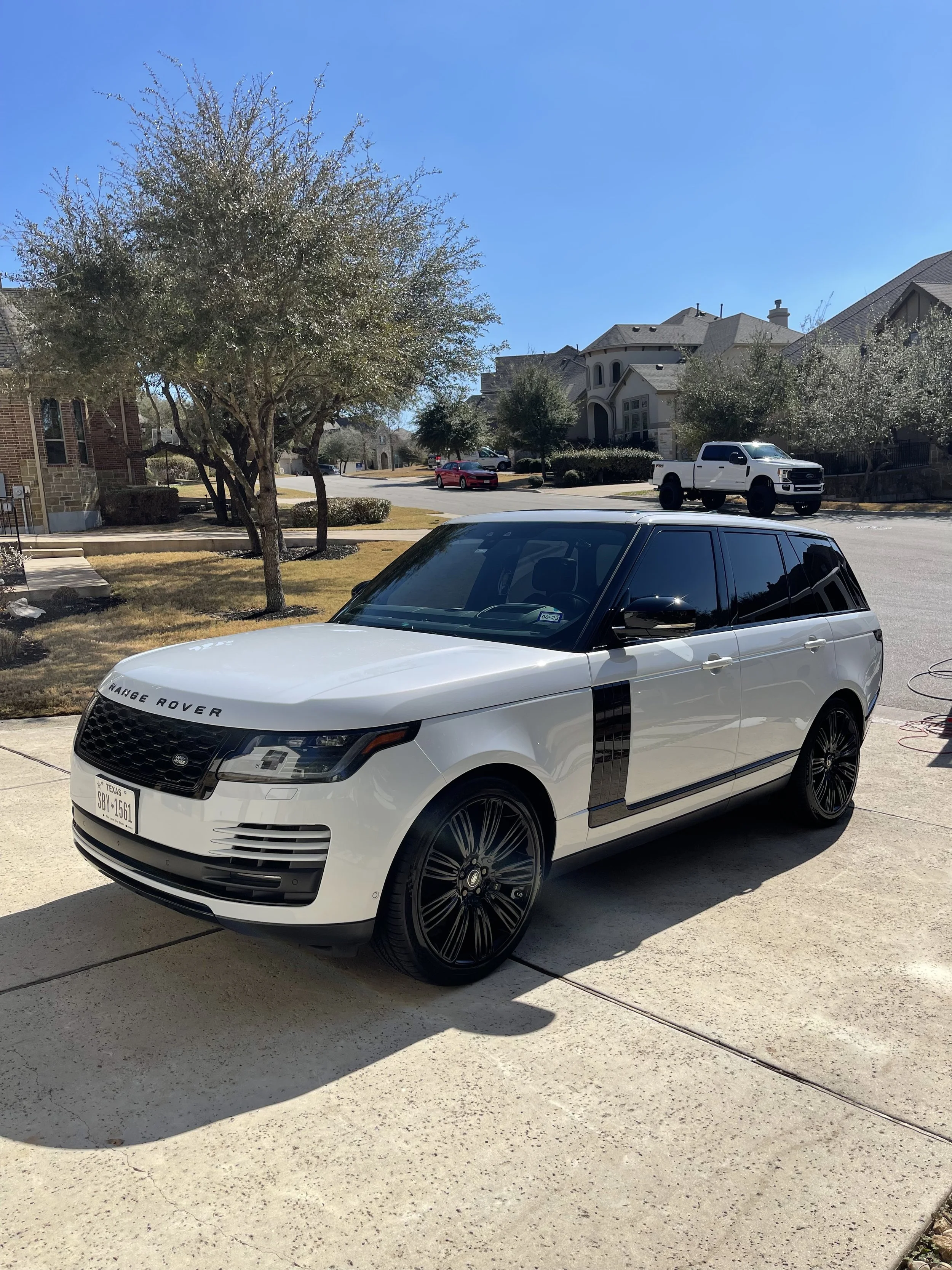 A white Range Rover with black tinted windows and black rims parked on a driveway in a suburban neighborhood.