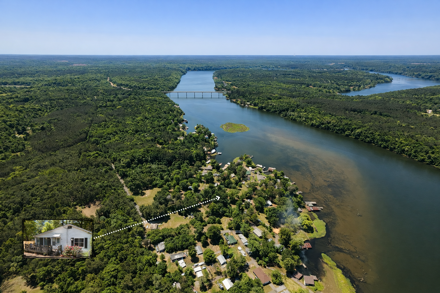 Aerial view of a river with a bridge, surrounded by lush green forest and a residential area along the shoreline. An inset shows a close-up of a white house with a deck and flowers.