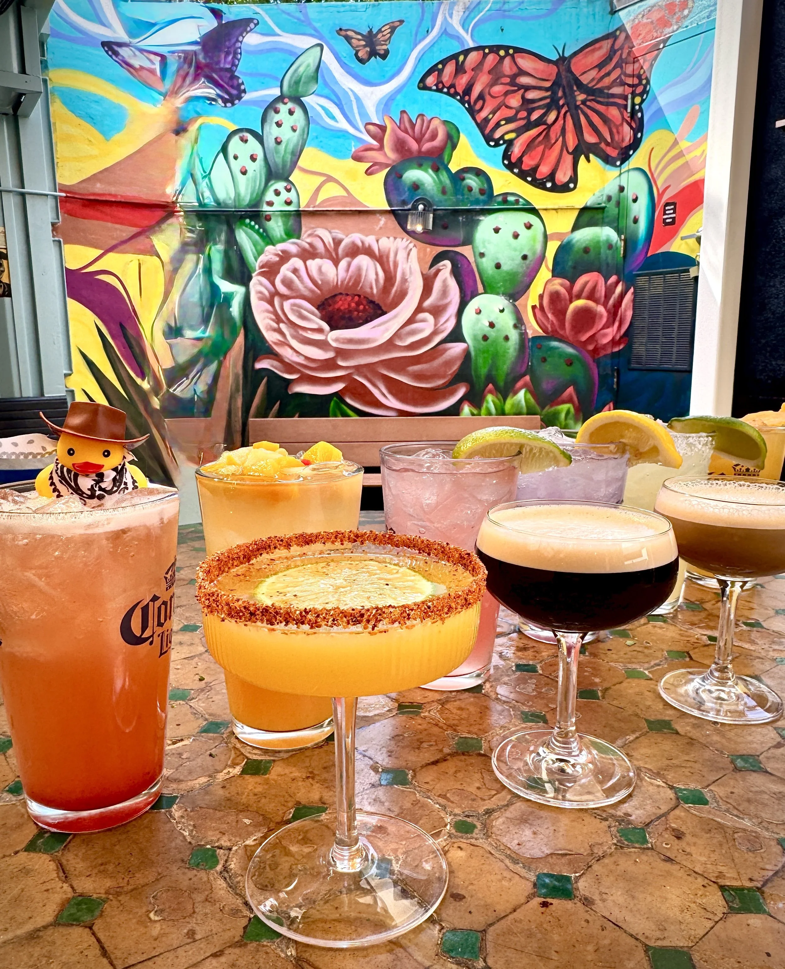 An array of colorful cocktails with a beautiful mural background in Washington DC on U Street