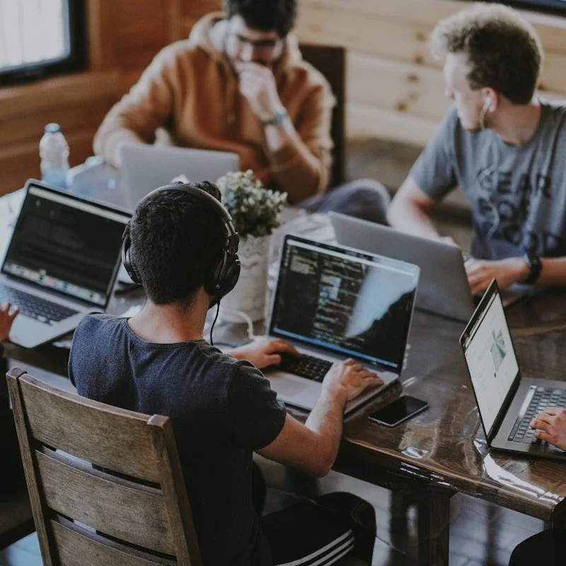 Squarespace website designer. A group of young people working on laptops at a wooden table in a cozy indoor setting with natural light.