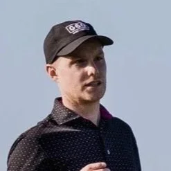Chris Rose from Strike Wedge. A young man wearing a black cap and a dark, patterned shirt outdoors against a light sky background.