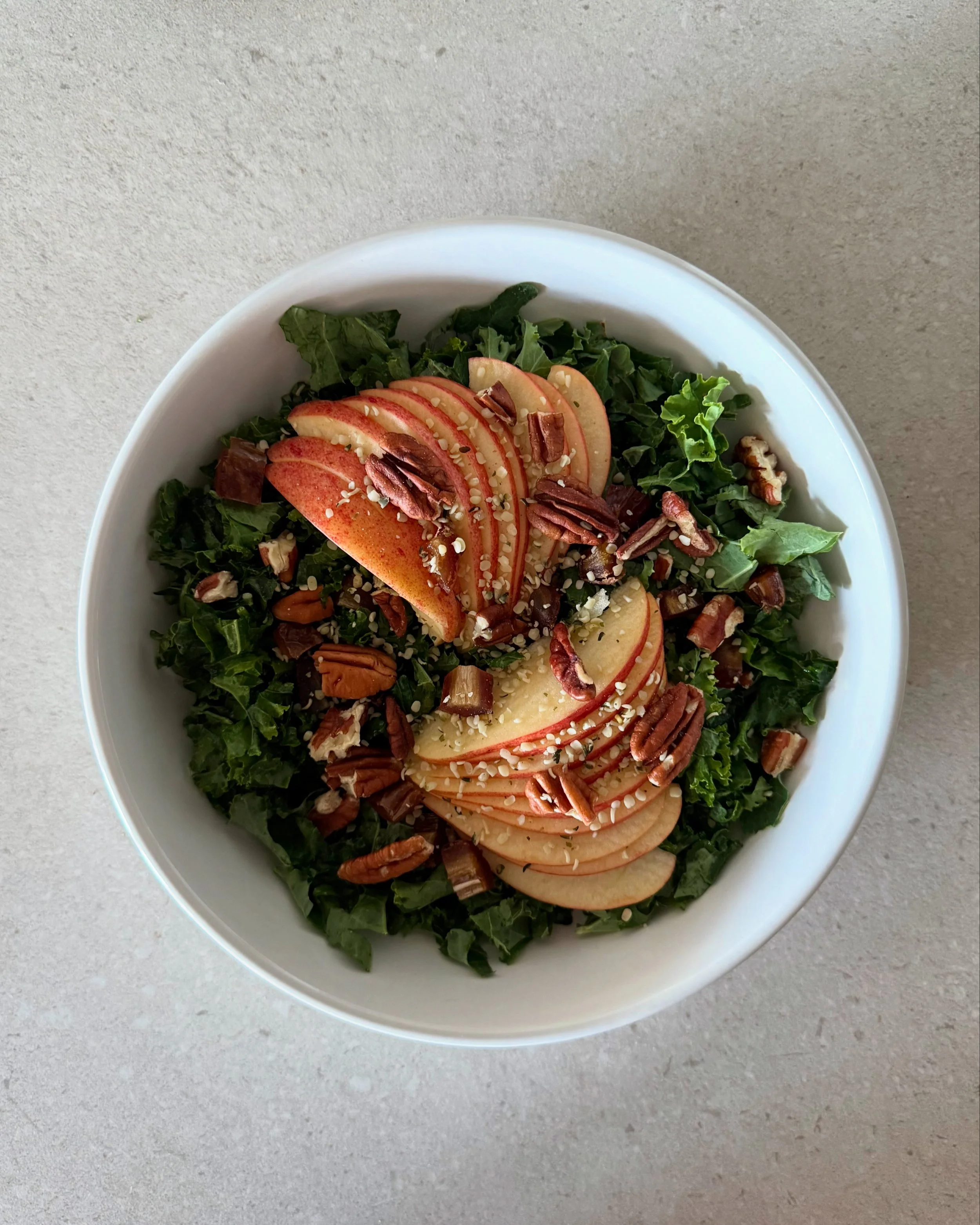 Bowl of mixed green salad with sliced apples, pecans, and shredded cheese.
