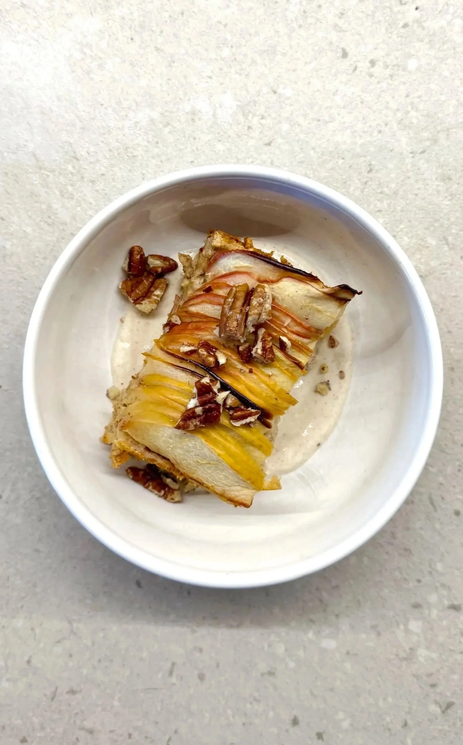 Sliced pear on a piece of bread topped with chopped pecans in a white bowl.