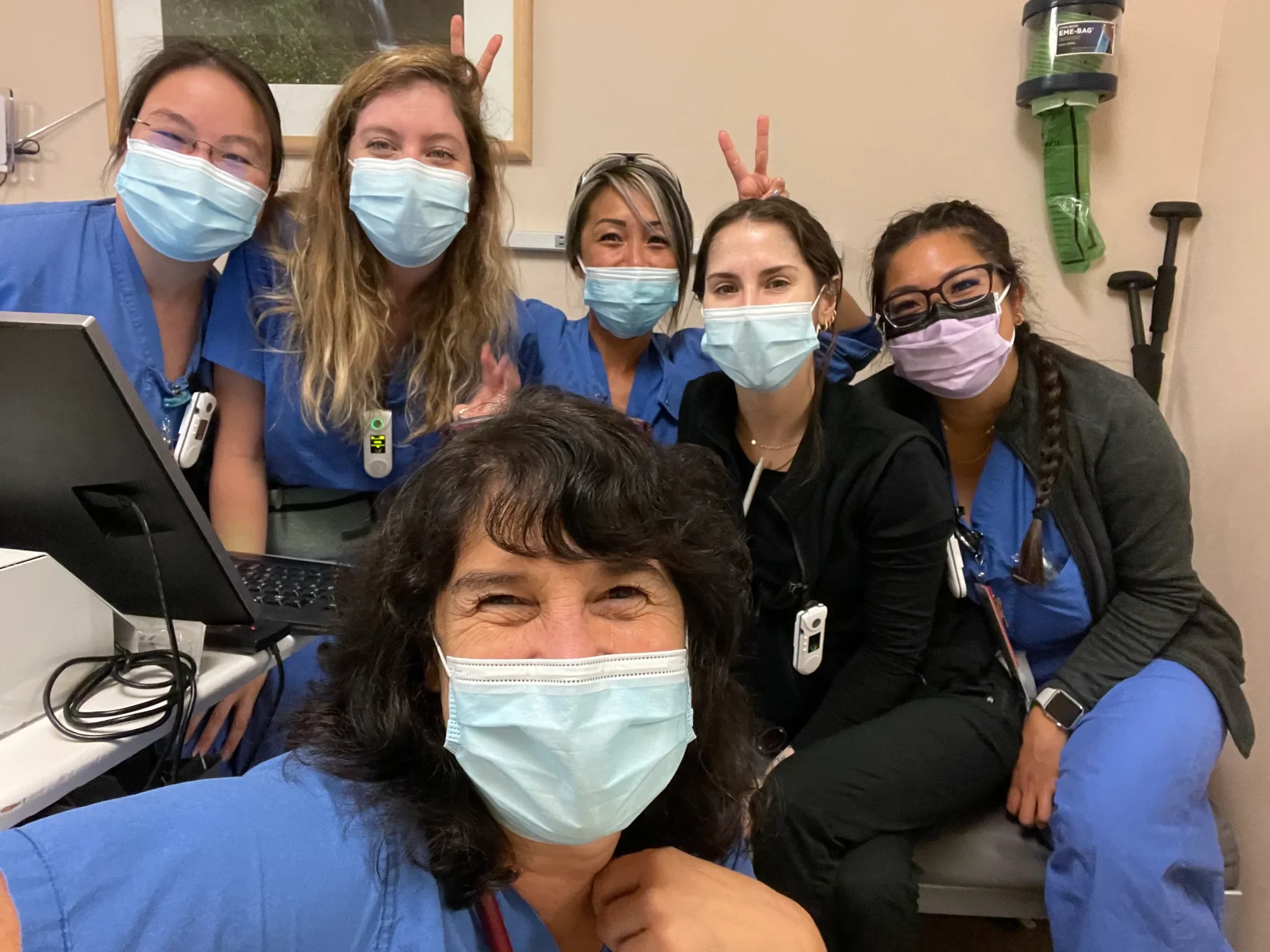Sharon Meieran & a group of healthcare workers wearing face masks, some making peace signs, in a hospital or clinic room.