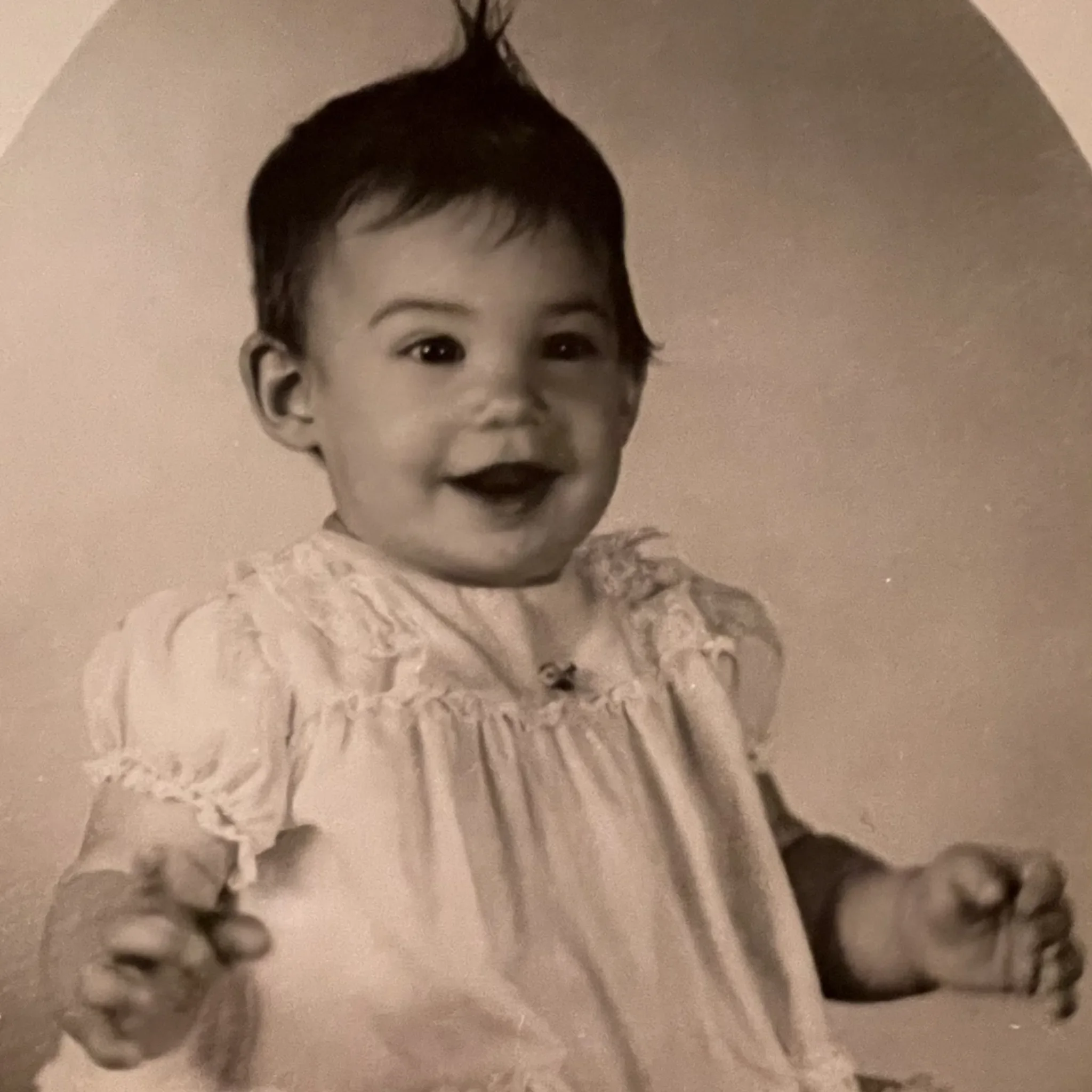 A black and white picture of a smiling Sharon Meieran wearing a lace dress, with short, dark hair in a blunt cut, against a plain background.