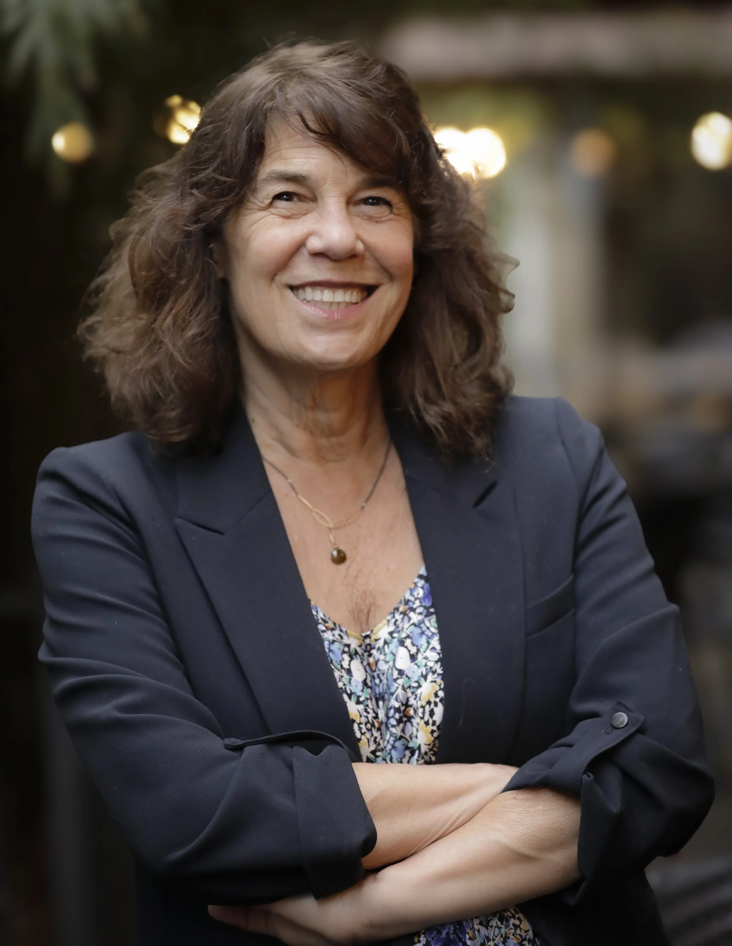 Dr. Sharon Meieran, candidate for Multnomah County Chair, standing with her arms crossed, blurred city lights in the background.