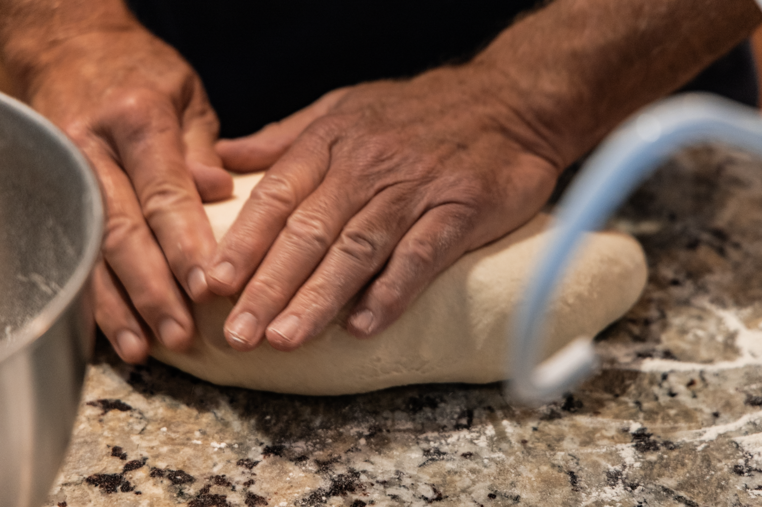 Hands kneading dough on a granite countertop.