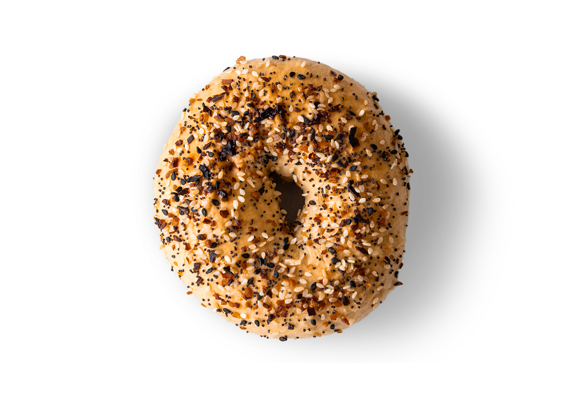 Close-up of a toasted bagel with cream cheese, topped with black sesame, white sesame, and crushed garlic, against a black background.