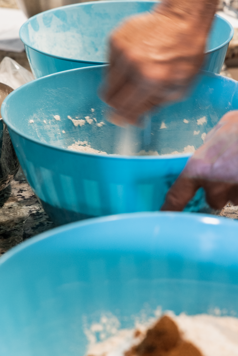 Person mixing ingredients in a blue bowl with a hand blender, with other blue bowls nearby, on a countertop.