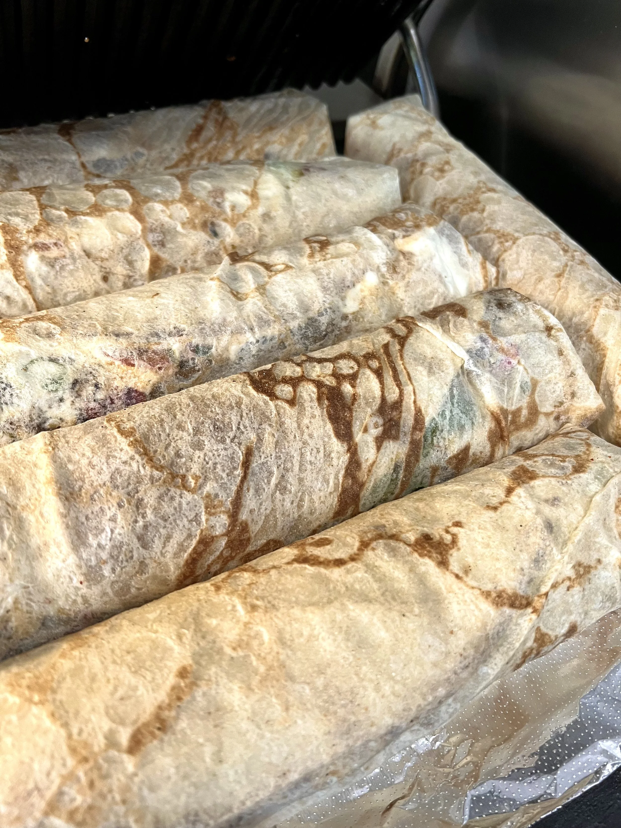 Close-up of several rolled futuristic marbled stone or mineral-like objects in shades of beige, brown, and cream, arranged in a row on a perforated metallic surface.