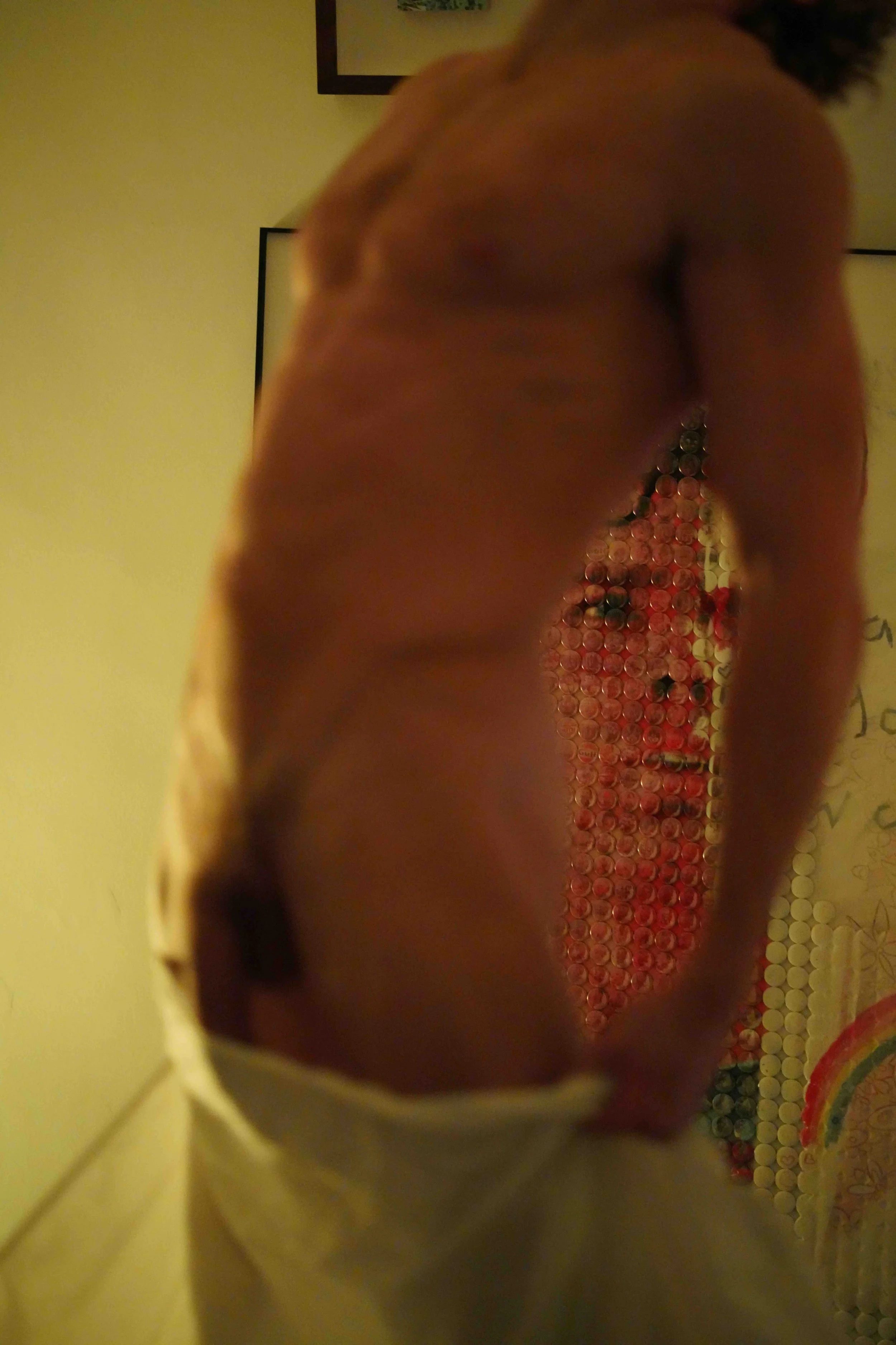 Close-up of a person's face with prominent forehead and neck, background showing a pattern of multicolored circular objects or beads, possibly part of an art piece or craft.