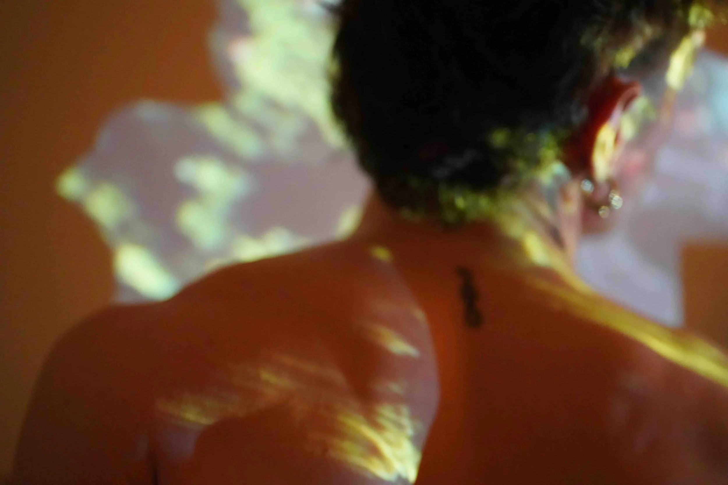 Close-up of a person's face with dark hair, possibly a woman, with bright light reflecting on the face, creating a blurred and abstract appearance.