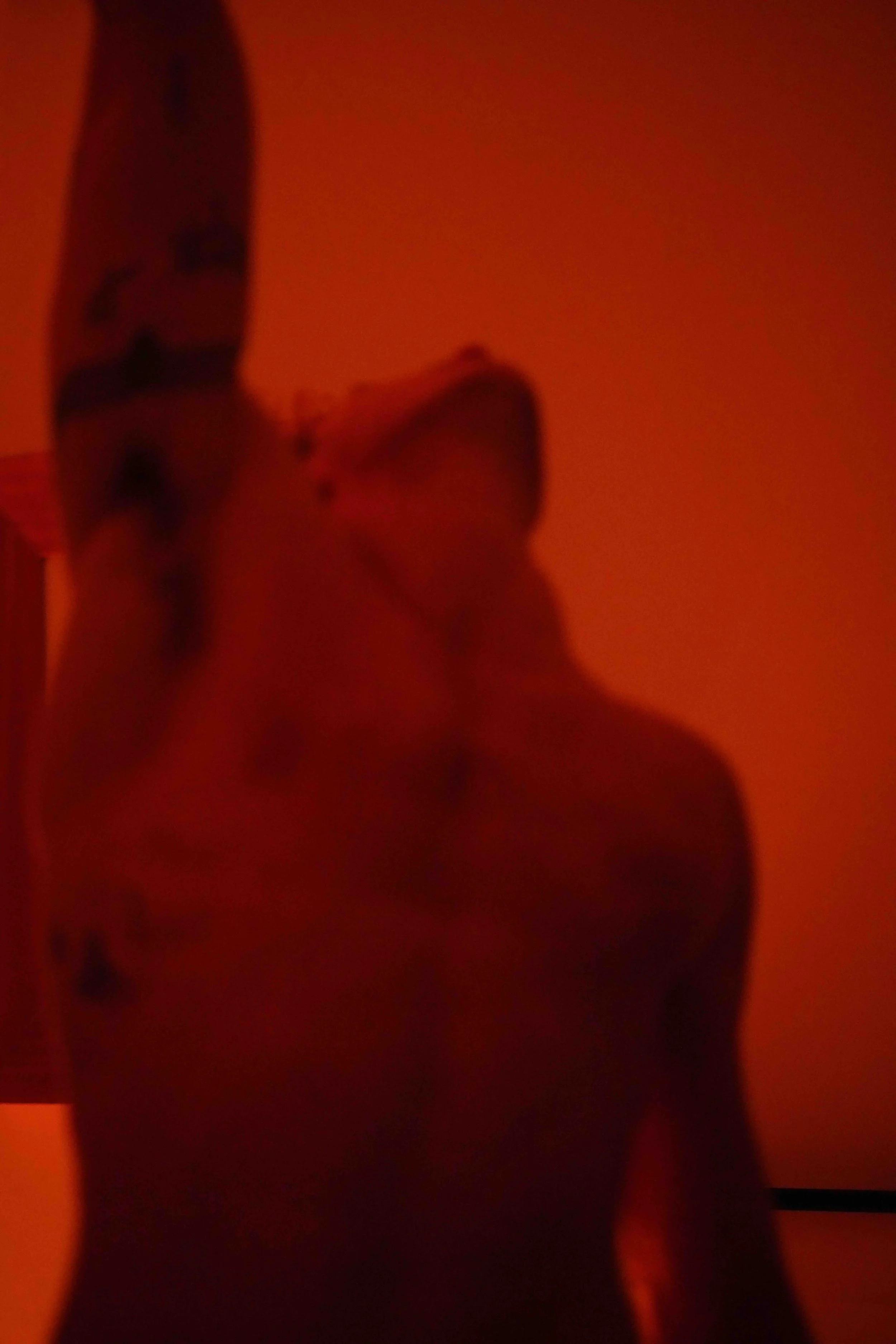 Blurry image of a person's body silhouette against a red or orange background, with one leg raised and foot pointing upward.