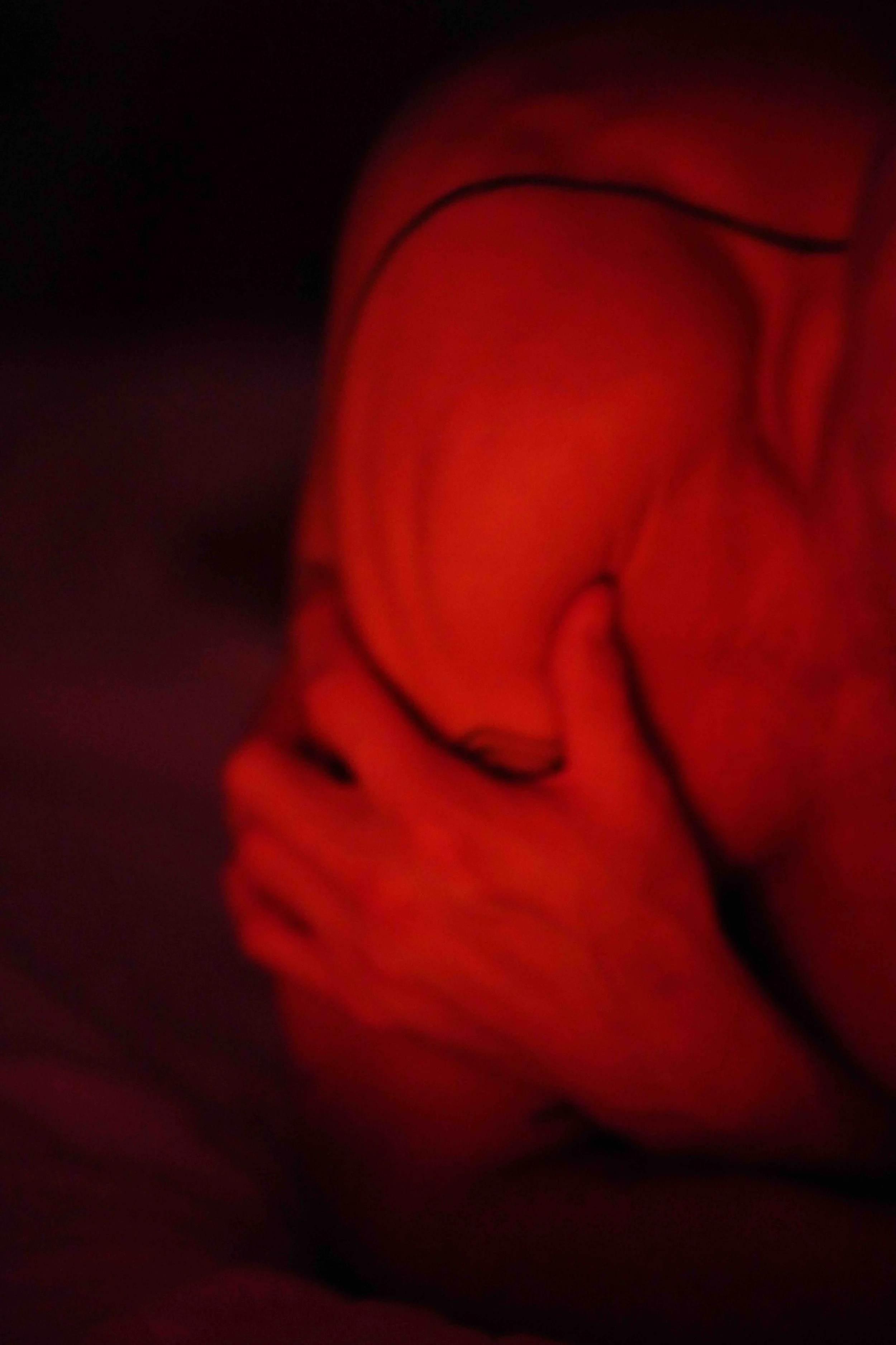 Close-up of a red rose with dark outlines, appearing abstract and blurry in a dark setting.