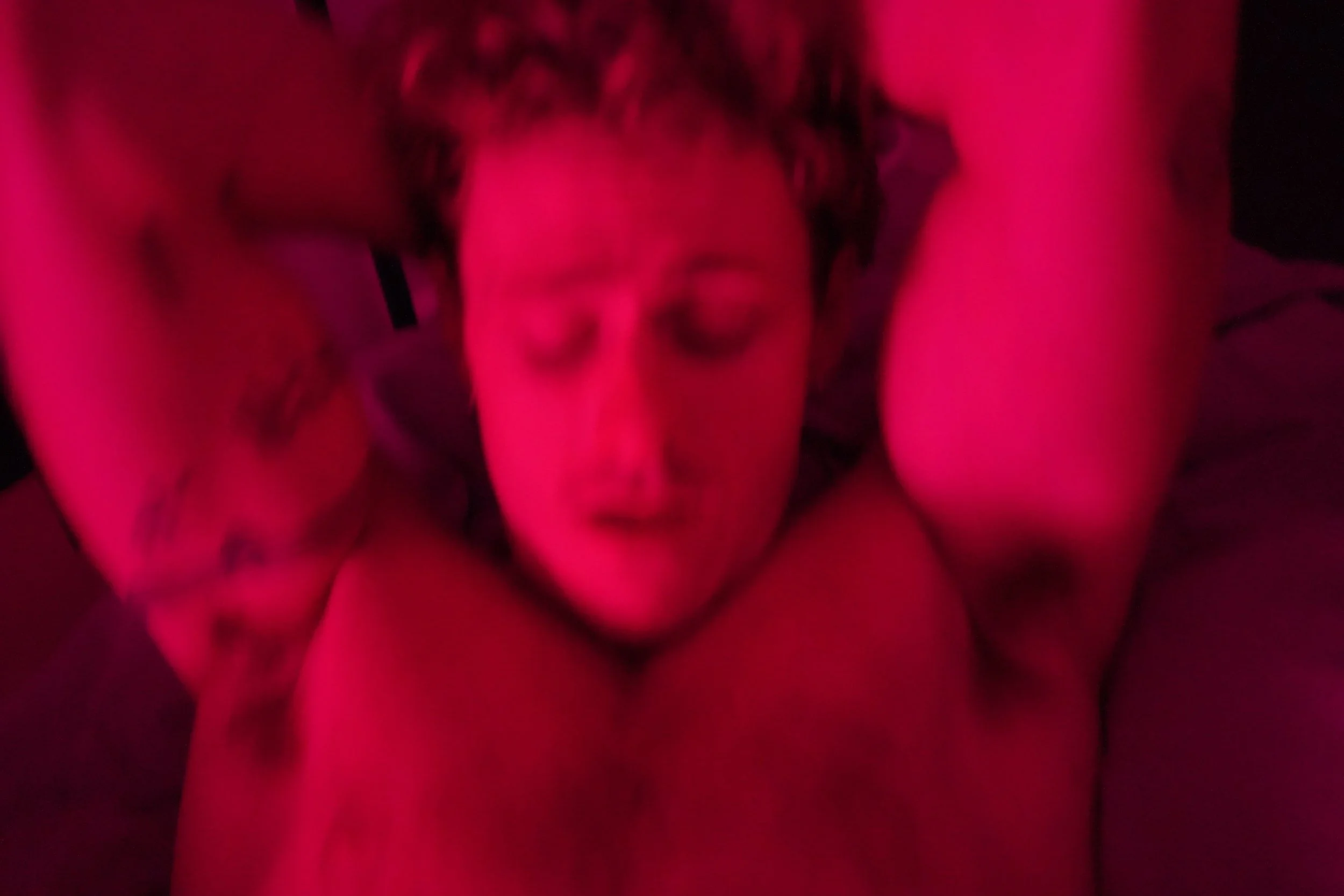 Close-up image of a woman with curly hair, with a pinkish-red lighting and blurred background.