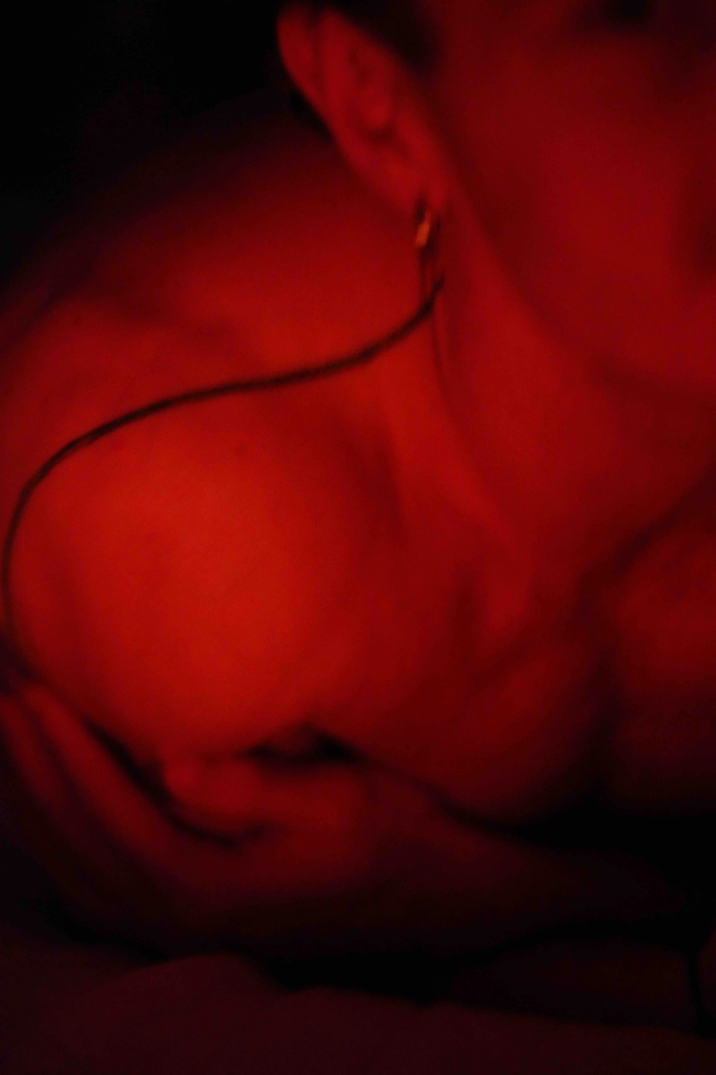 A close-up of a person's face with a warm red lighting, showing their eye, nose, and mouth, with a focus on the eye and lips.